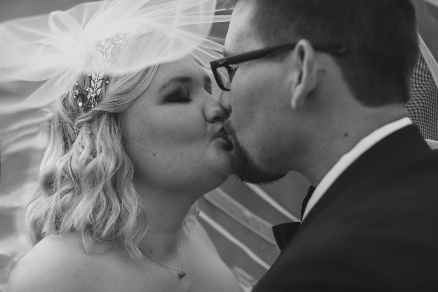 Black and white photo of the bride and groom kissing through her veil