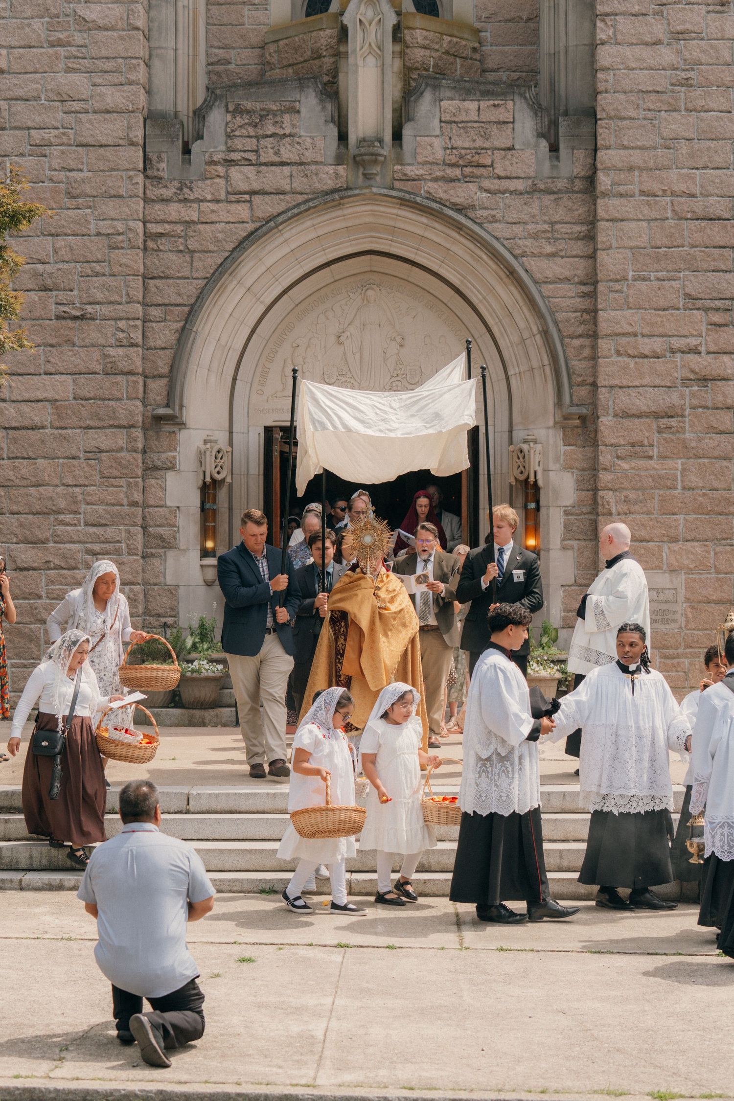 Priest with the monstrance under a canopy on the church steps, surrounded by altar servers