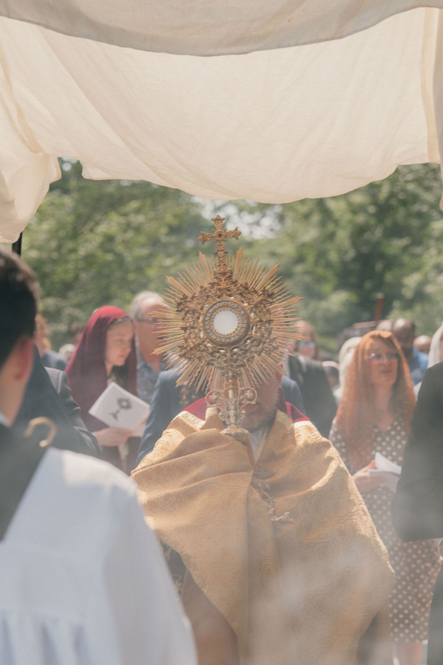 Priest blessing the faithful with the monstrance under a canopy during a Corpus Christi procession