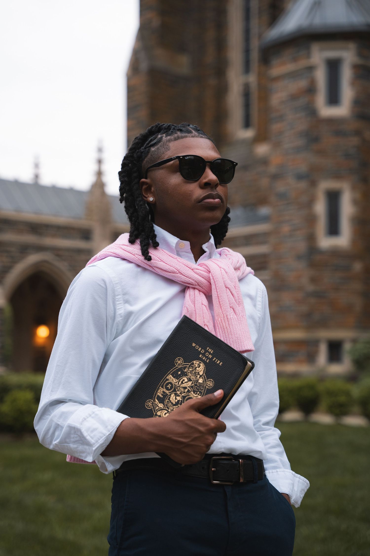 Graduate in sunglasses holding a Bible in front of Gothic stone architecture