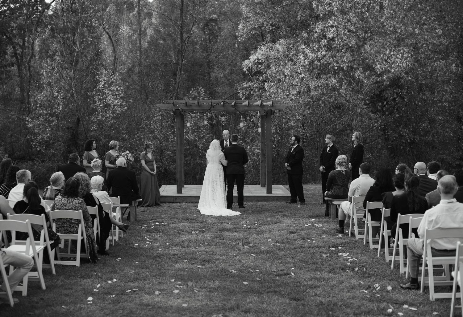 Black and white wide shot of an outdoor wedding ceremony in the woods