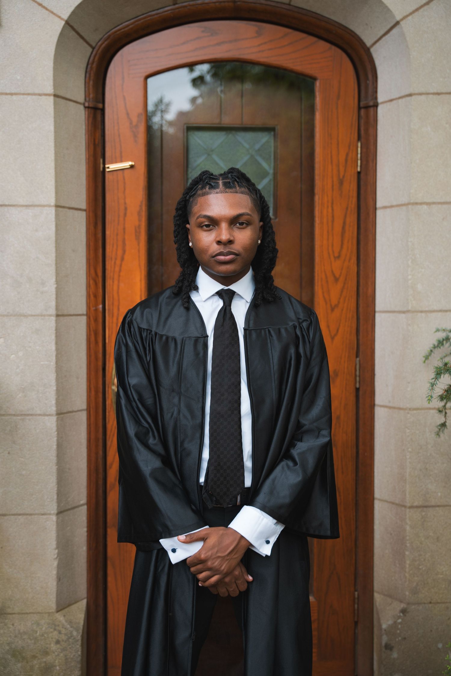 Graduate in a black gown standing in an arched wooden doorway