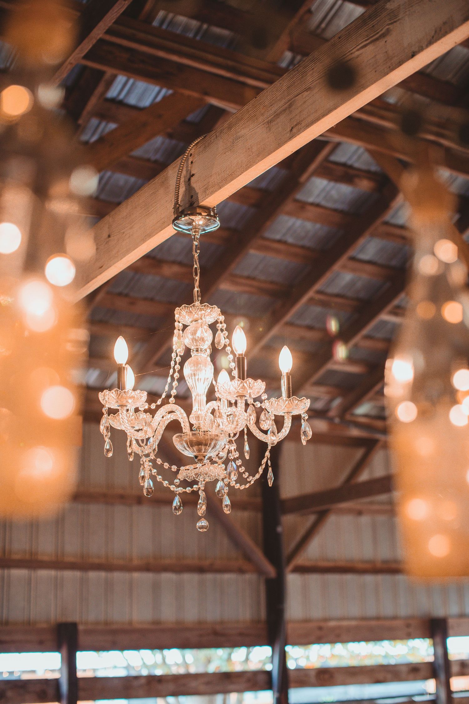Crystal chandelier hanging from the wooden beams of a barn wedding venue