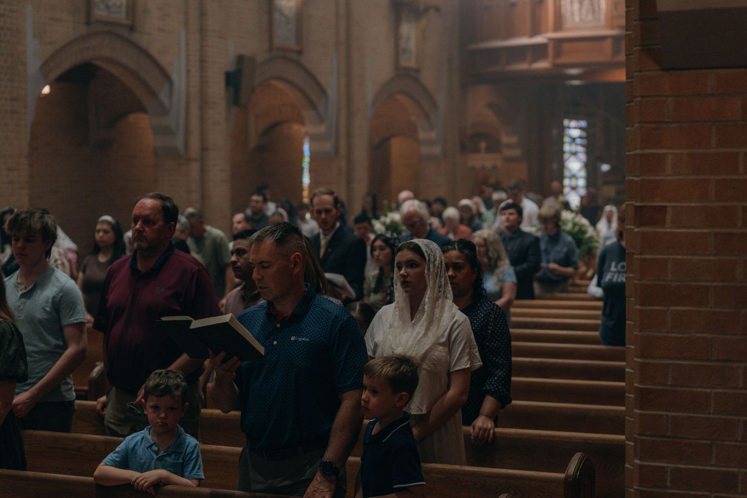 Congregation standing in wooden pews inside a historic church during Mass