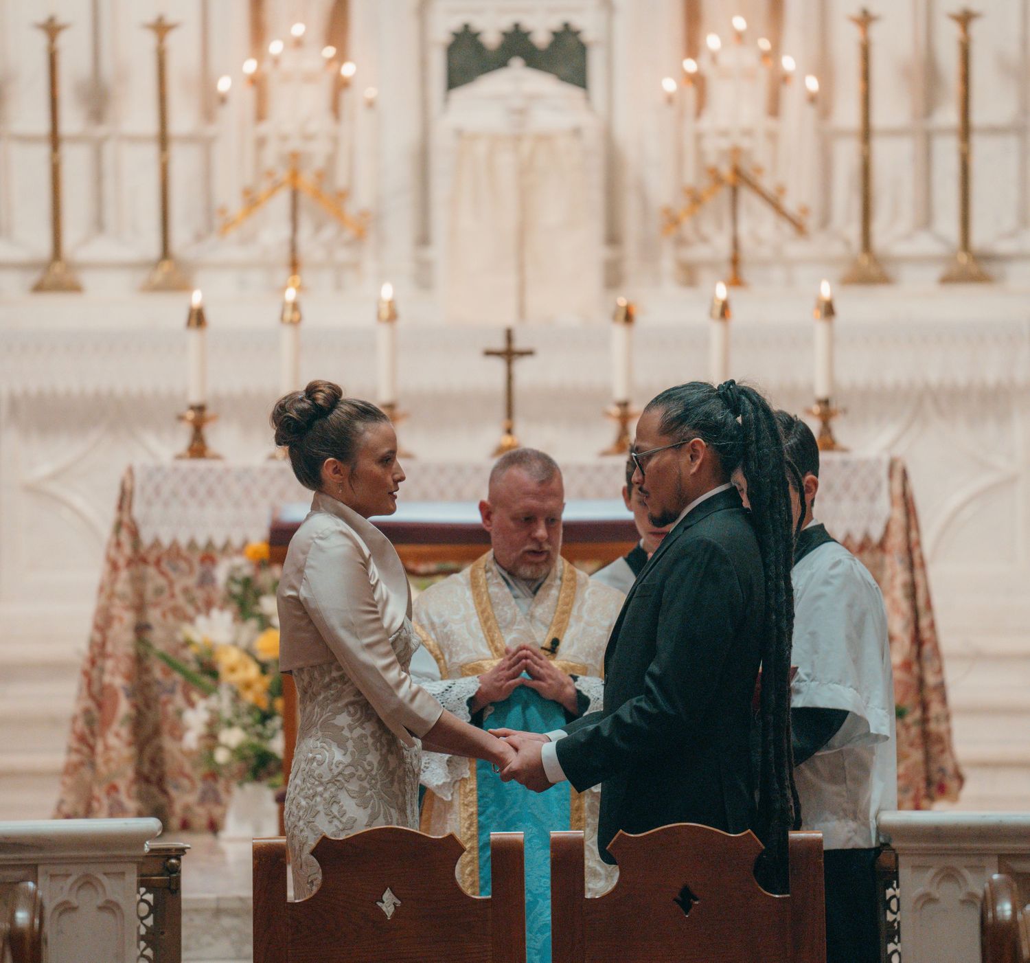 Priest blessing the bride and groom as they exchange vows at a Catholic altar