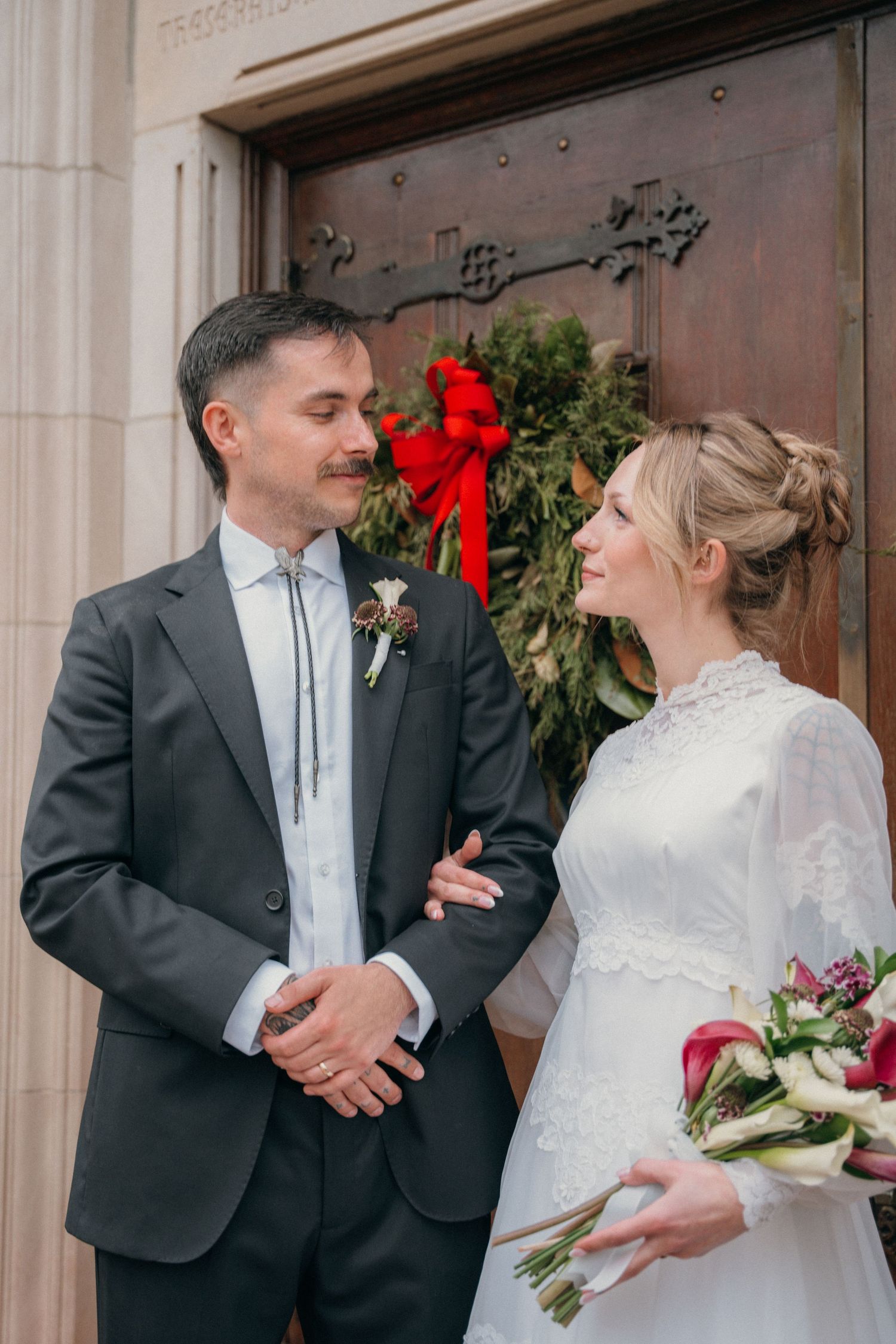 Bride holding red roses and smiling at the groom at the church doors