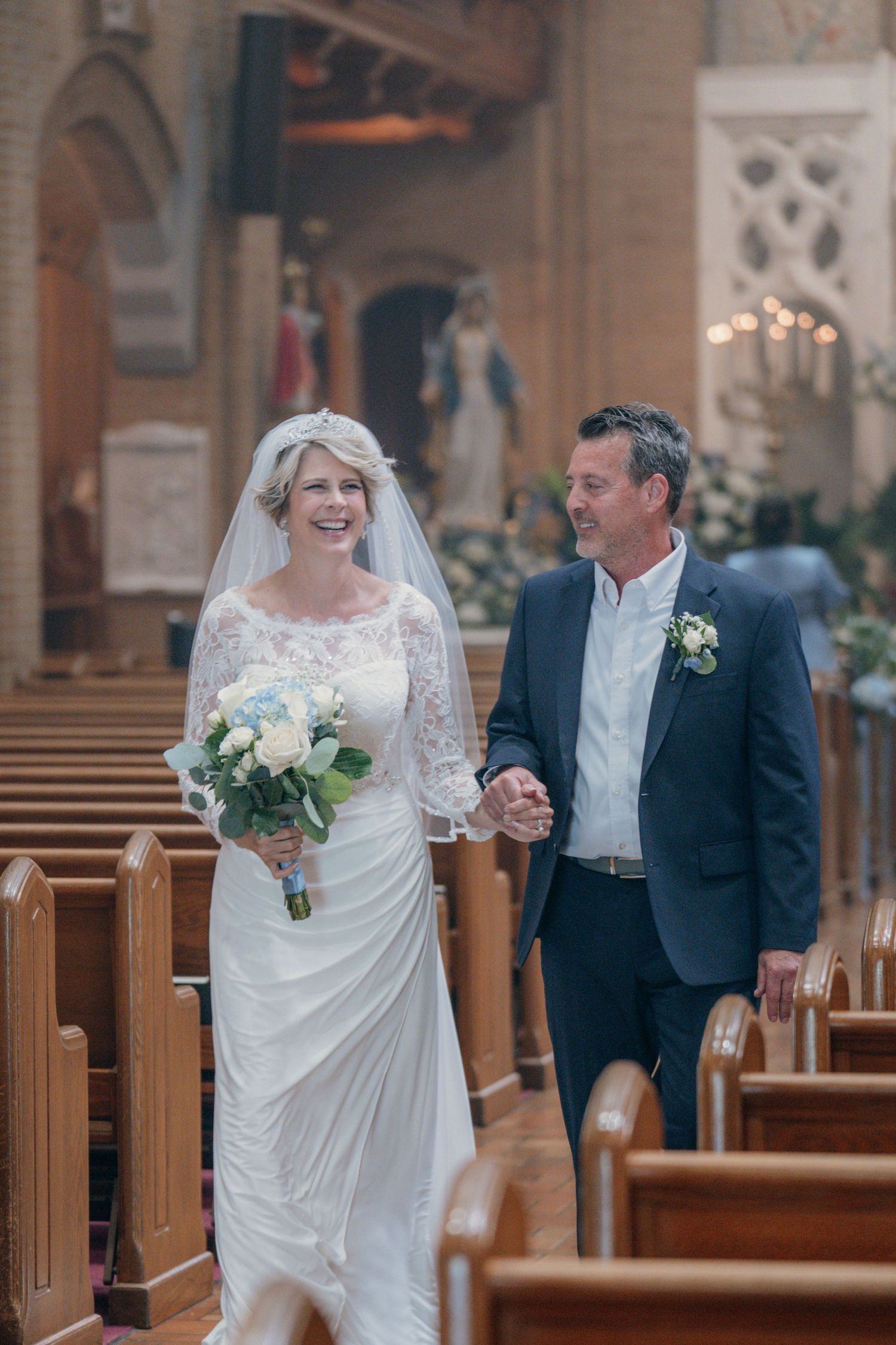 Father escorting the bride in a lace veil down the church aisle