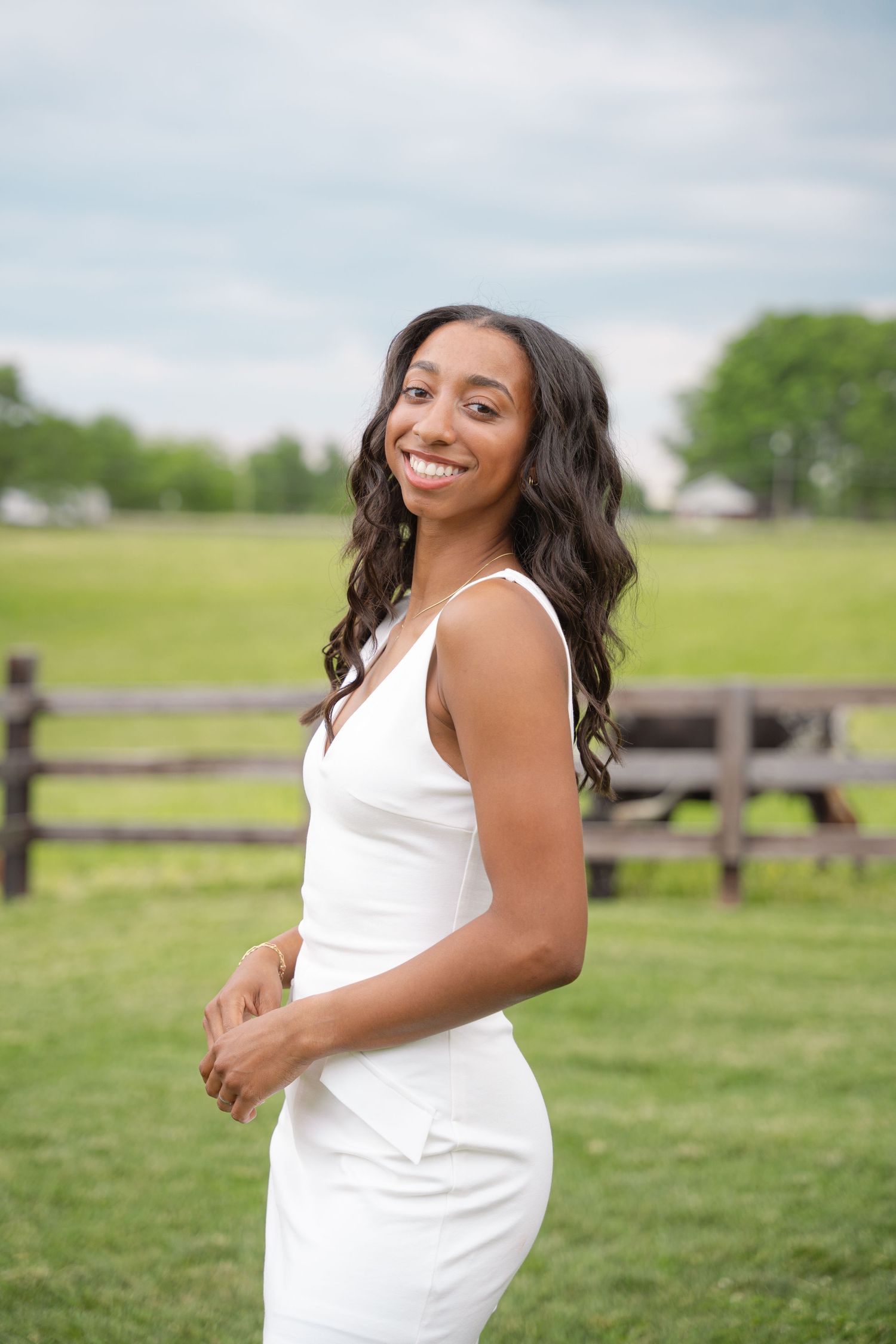 Senior portrait of a graduate in a white dress in an open farm field