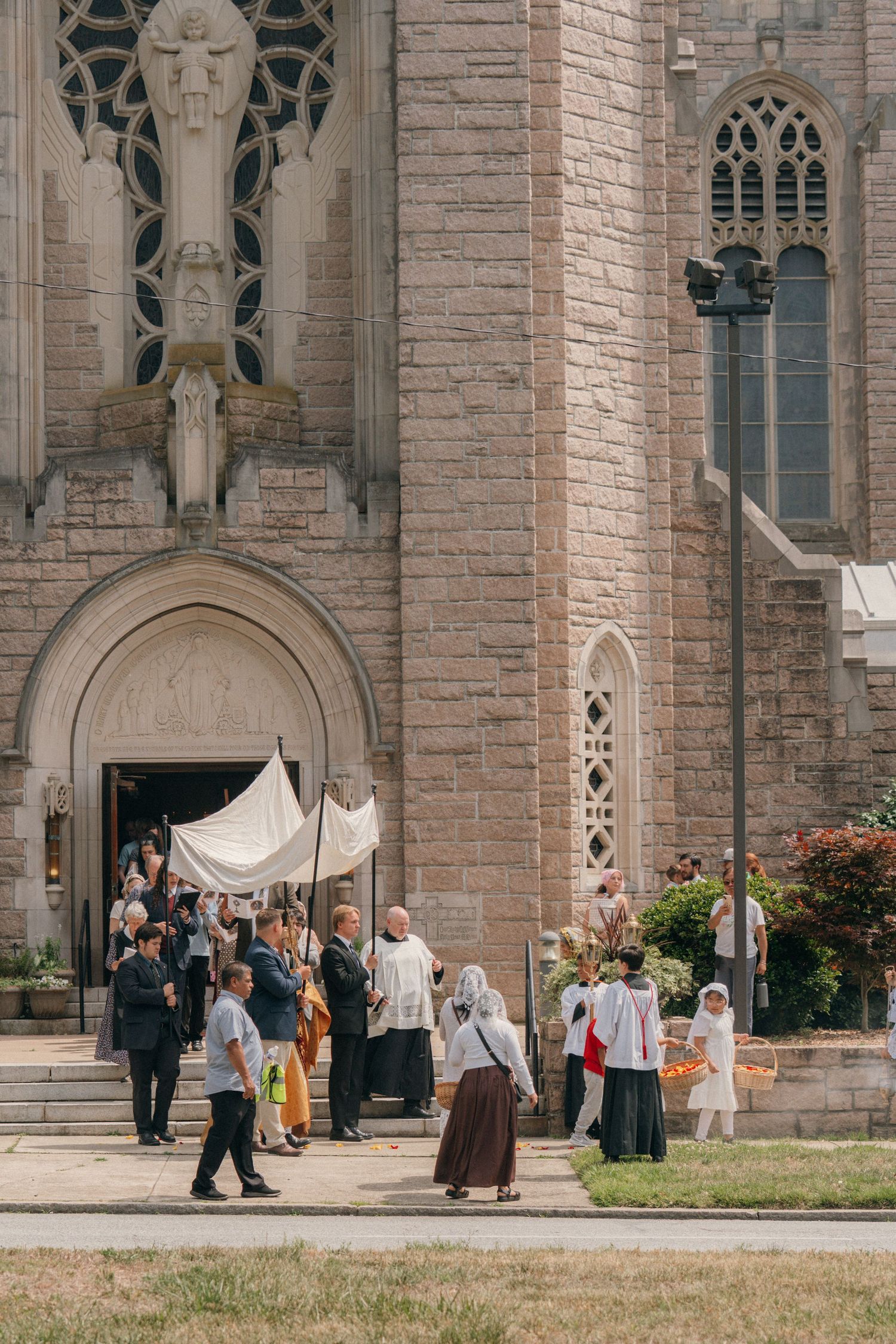 Corpus Christi procession emerging from the arched doors of a Gothic stone church