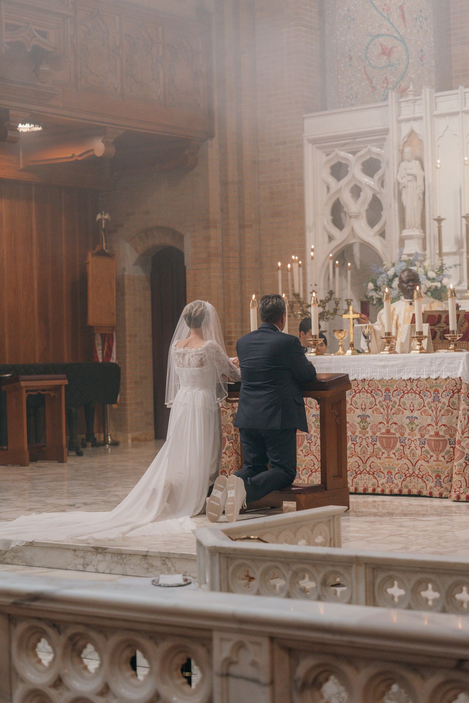 Couple kneeling at the altar in soft incense haze during their wedding Mass
