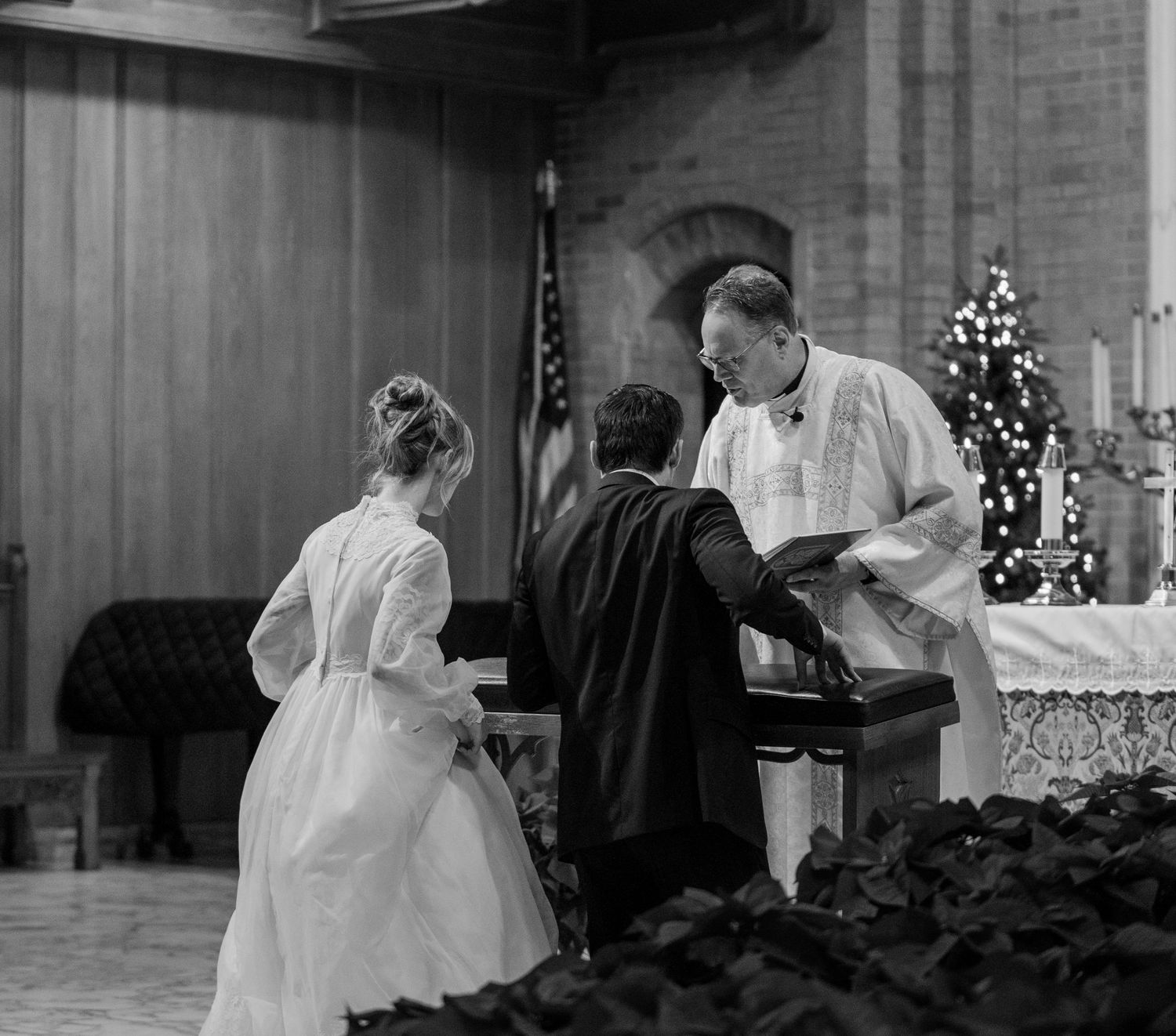 Black and white photo of the priest and couple at the altar during the vows