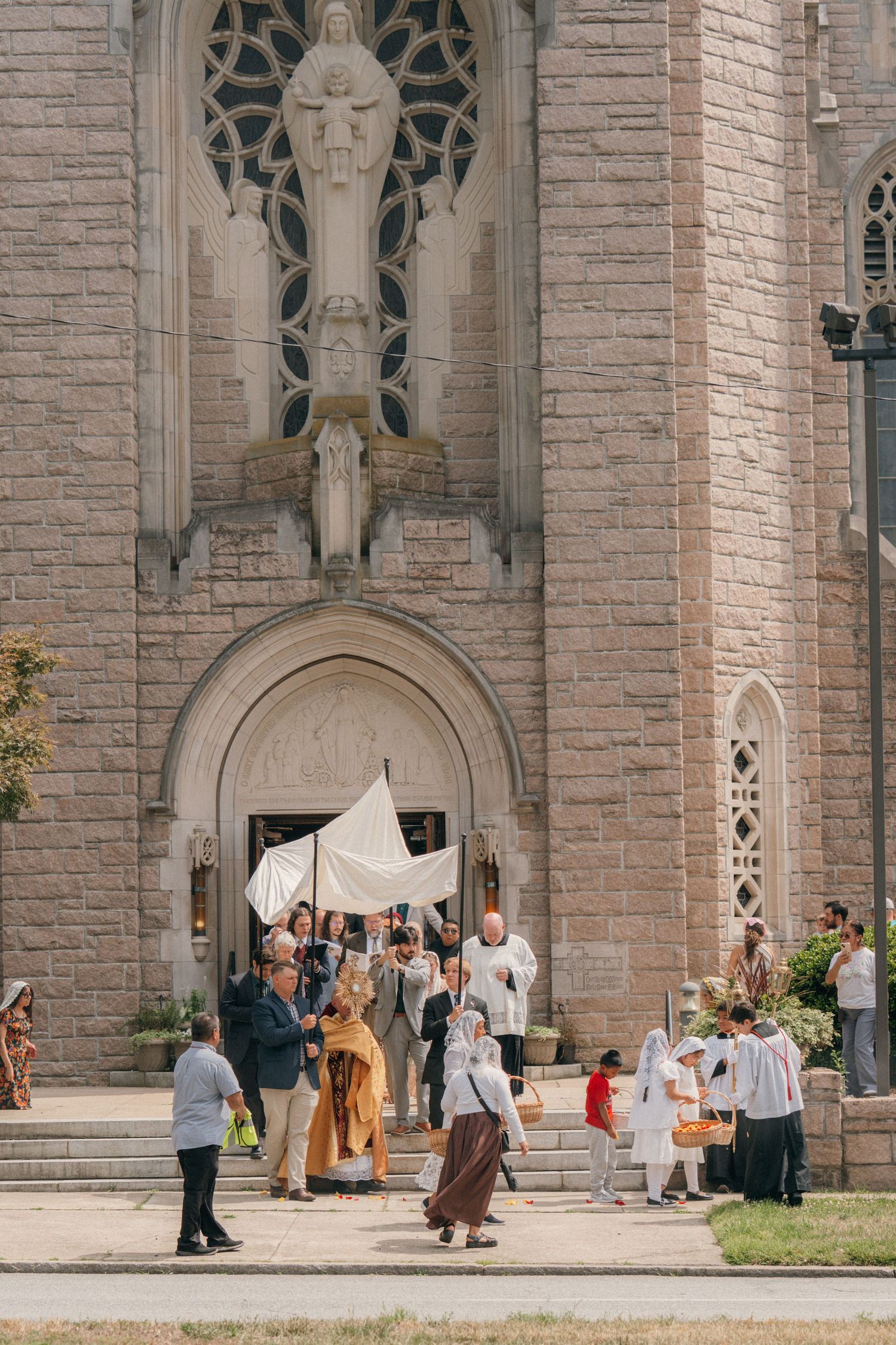 Gothic stone church facade with a Eucharistic procession and canopy gathered at the entrance