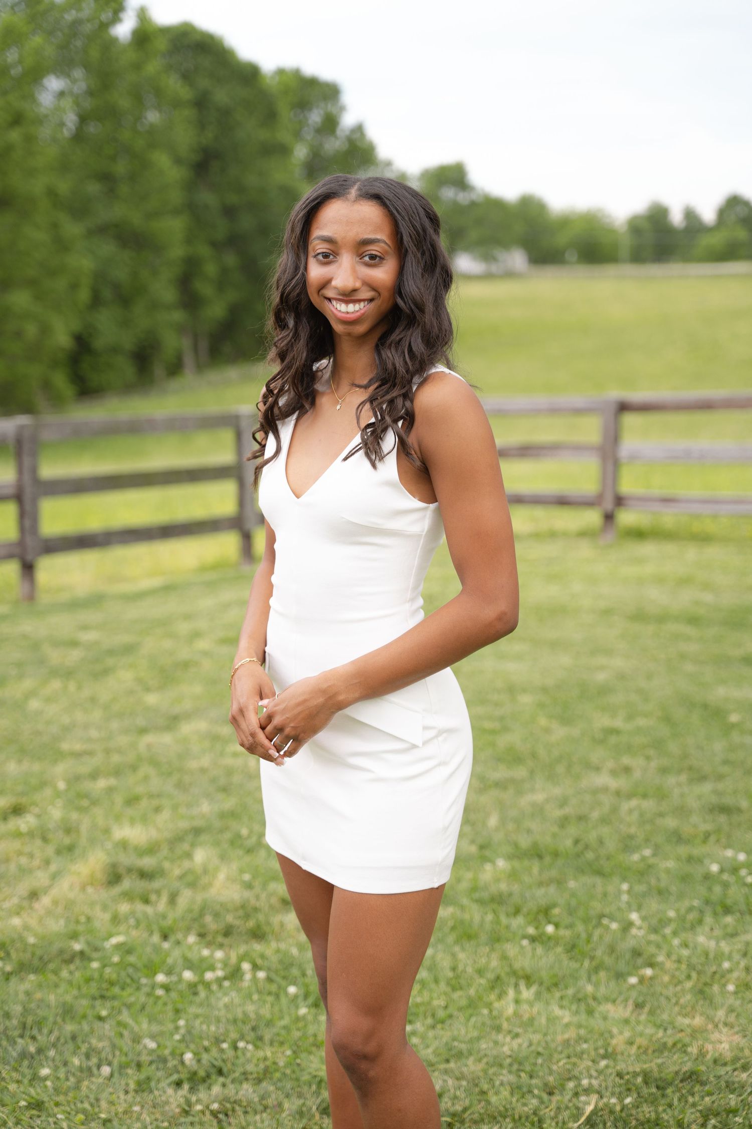 Full-length graduation portrait of a young woman in a white dress on a farm