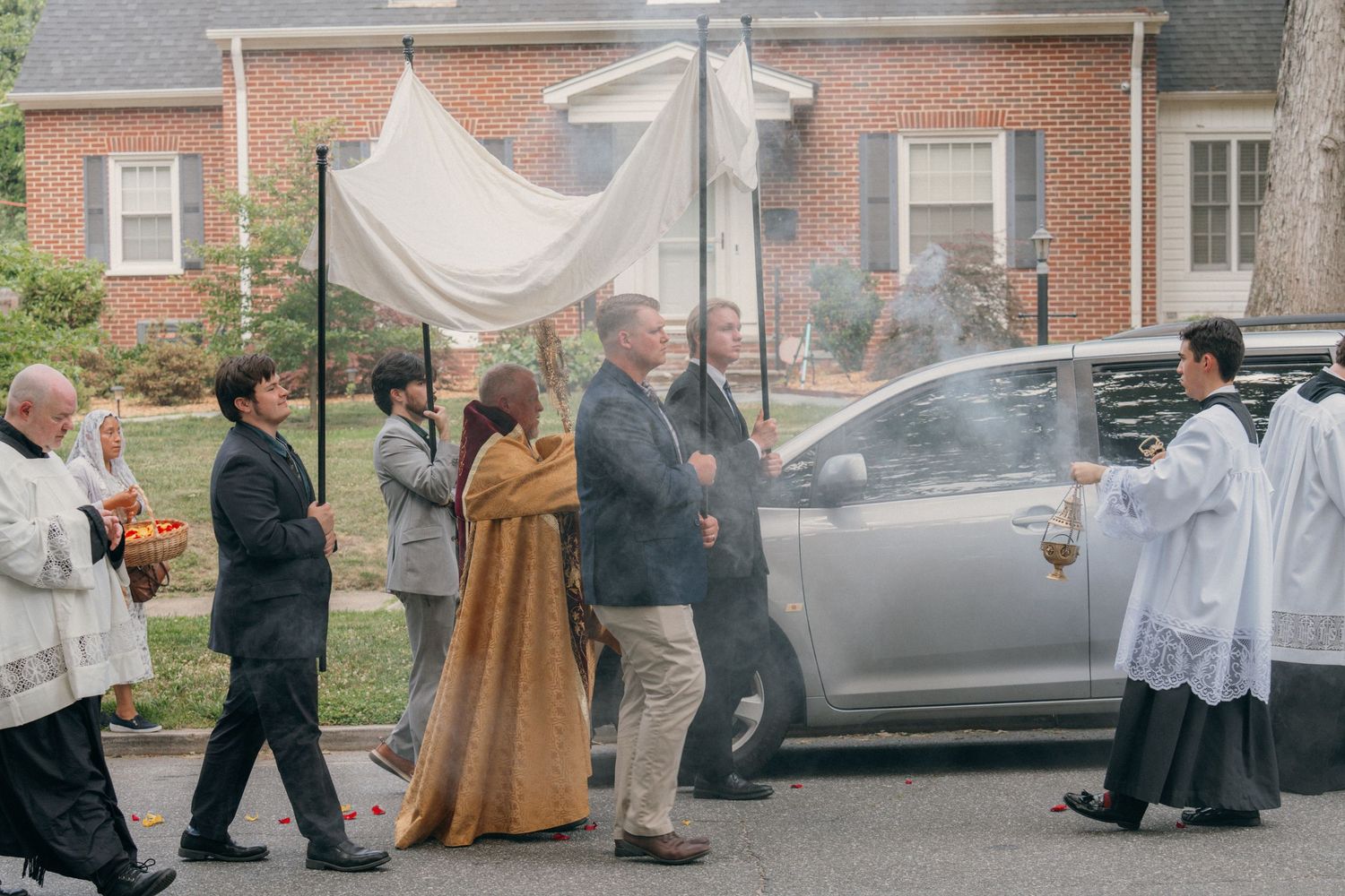 Corpus Christi procession passing a brick home on a neighborhood street