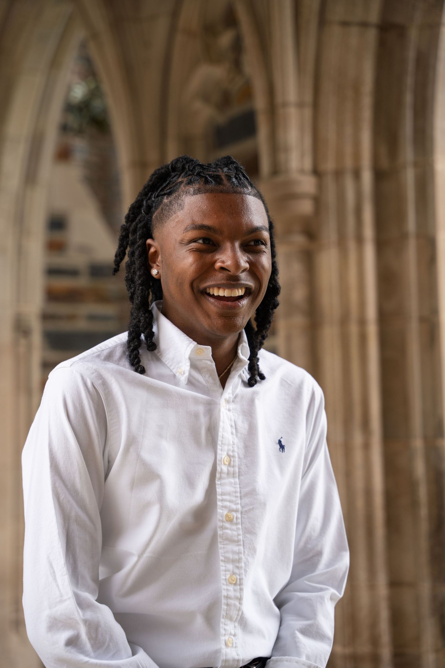 Smiling graduate in a white button-down shirt in a Gothic cloister