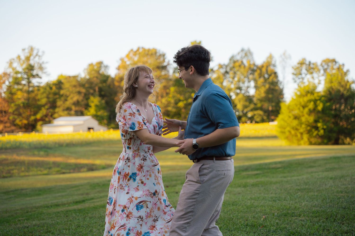 Engaged couple dancing playfully in a grassy field at golden hour