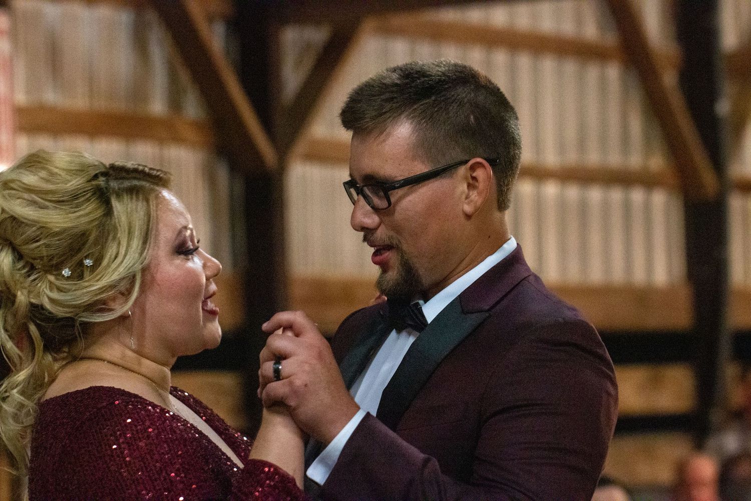 Groom smiling as he dances with a guest in a burgundy dress at the reception