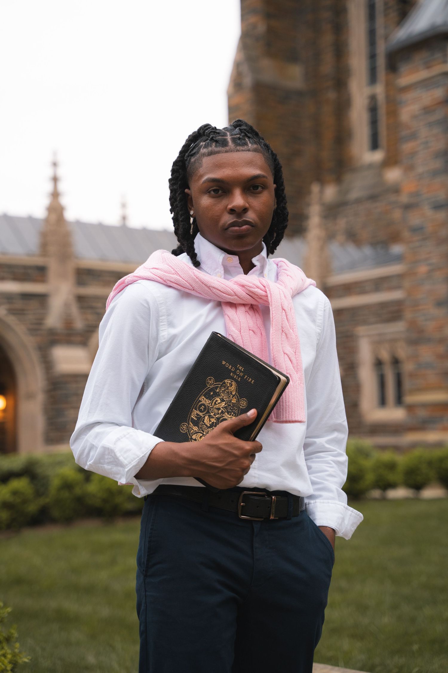 Graduate in a white shirt and pink sweater holding a Bible in front of a Gothic chapel