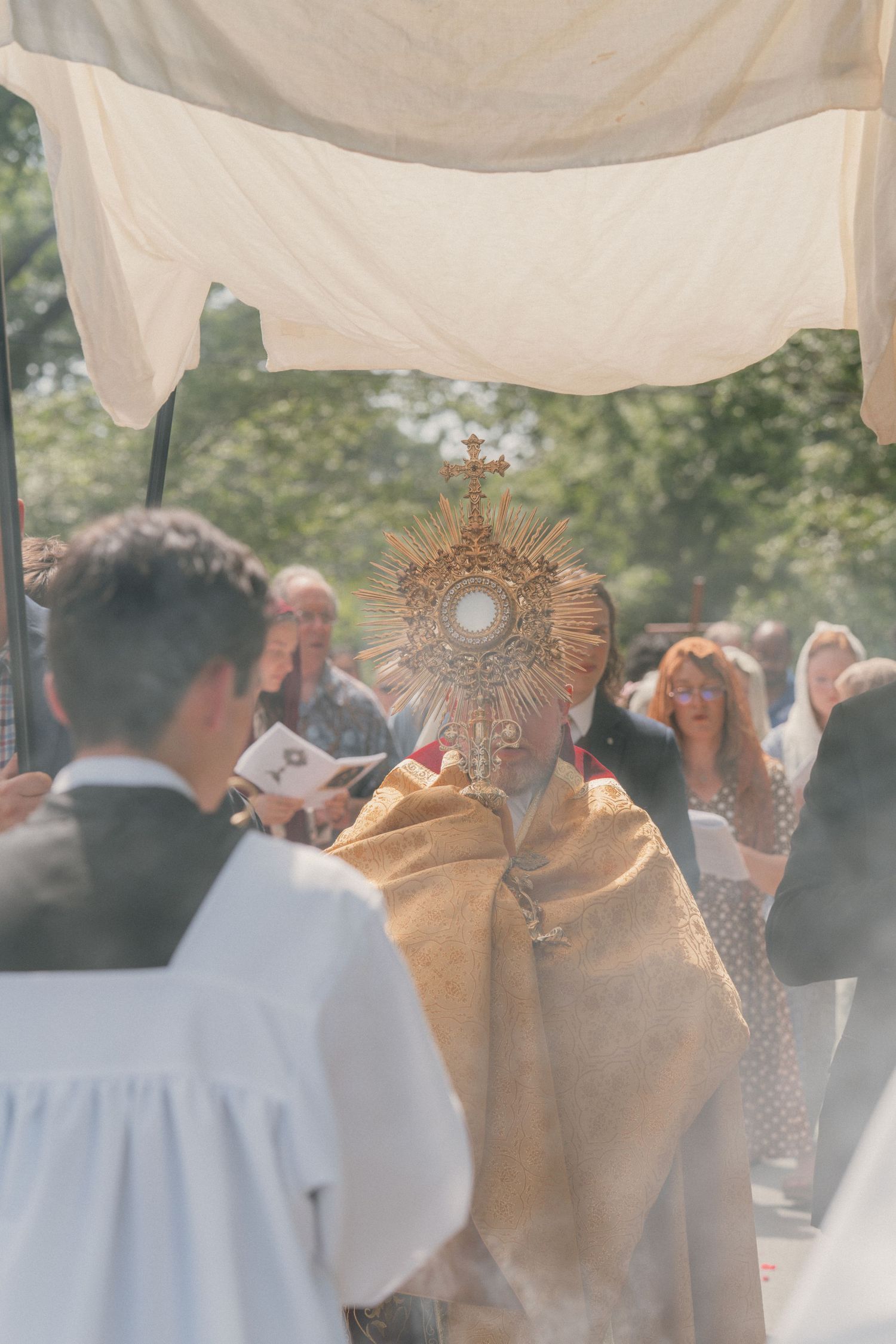 Altar servers in cassocks and surplices near the monstrance amid incense during Corpus Christi
