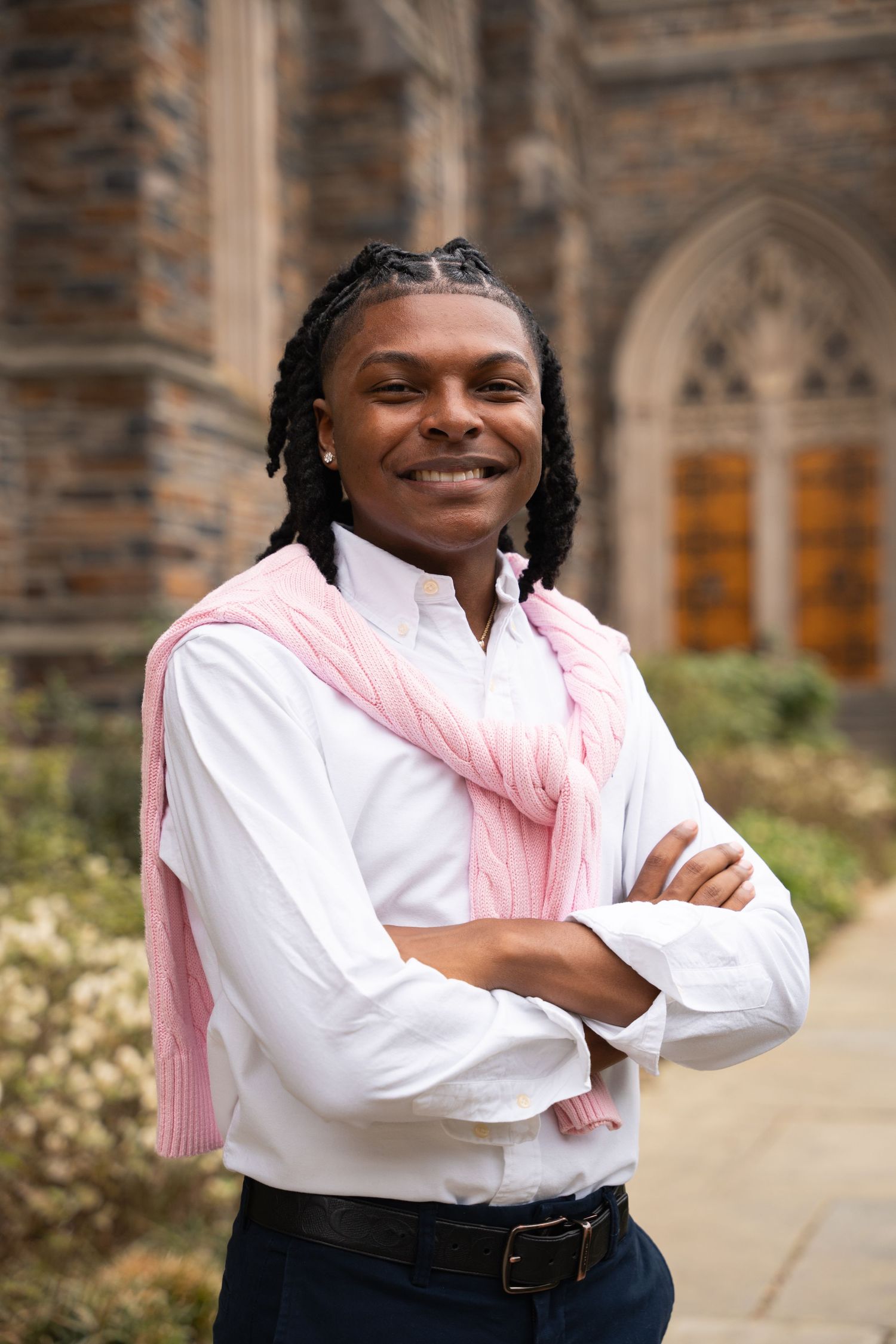 Smiling graduate with arms crossed in front of Gothic chapel windows