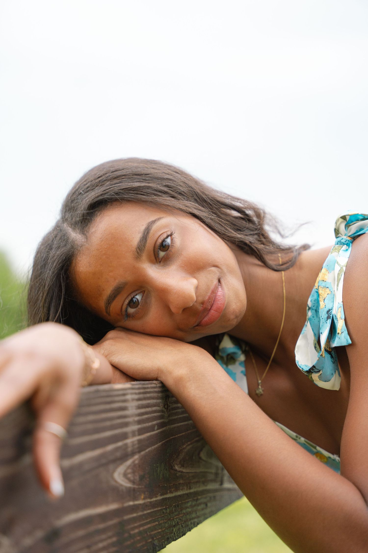 Close-up senior portrait of a young woman resting her head on a wooden fence rail