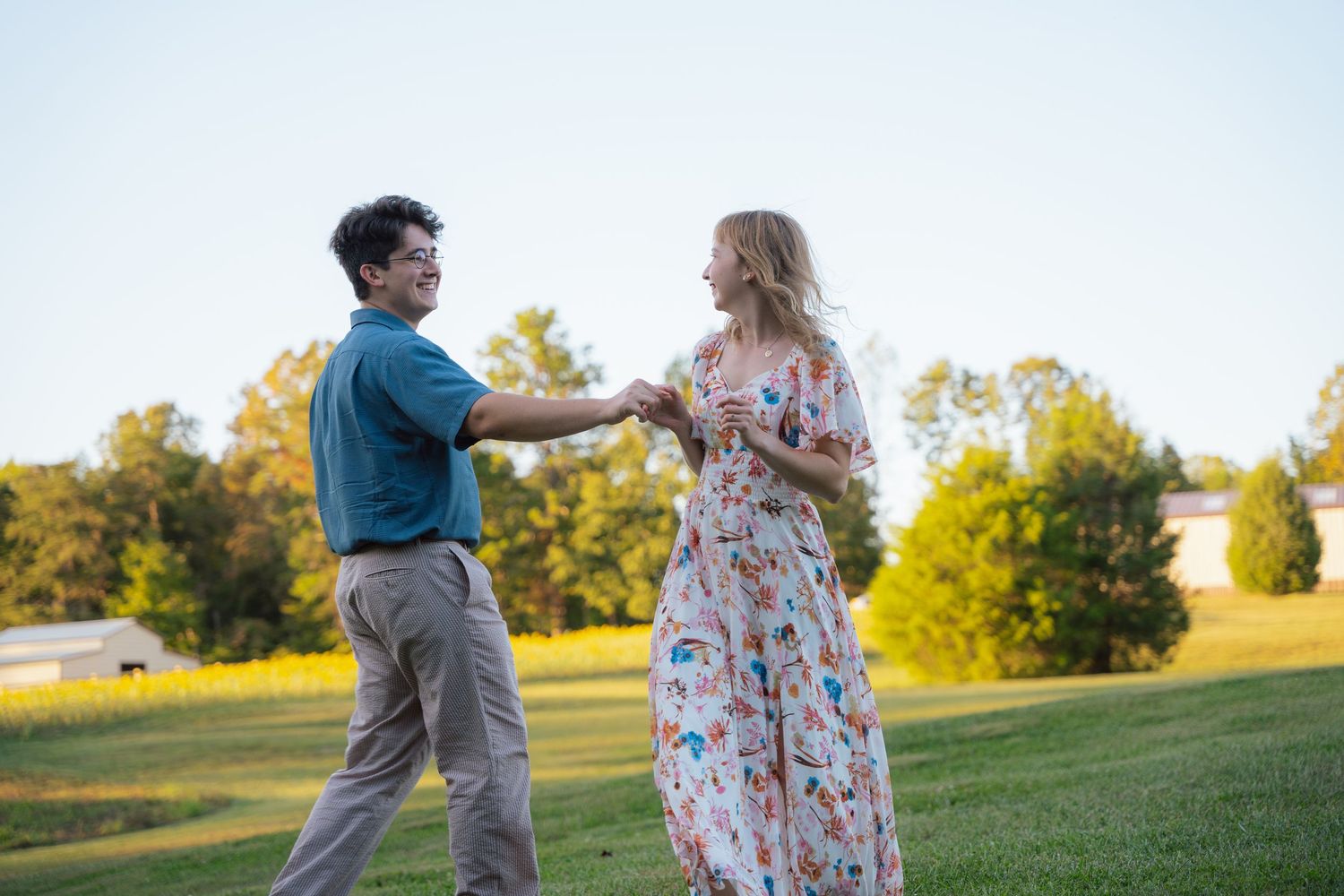 Couple holding hands and dancing in an open field at sunset