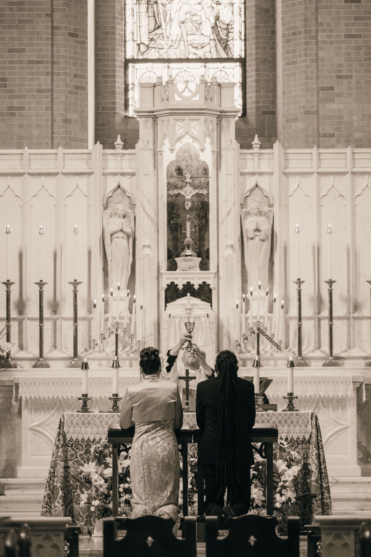Couple kneeling at the altar rail beneath an ornate white high altar