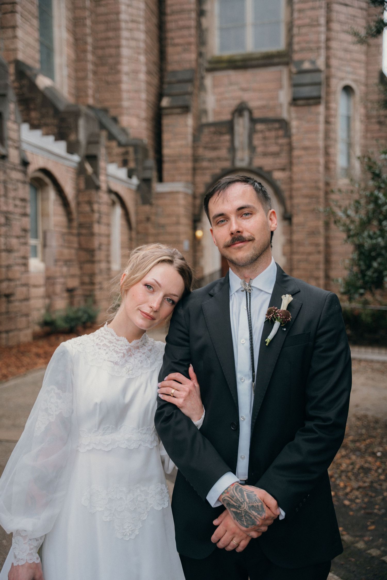 Bride resting her head on the groom's shoulder outside a stone church
