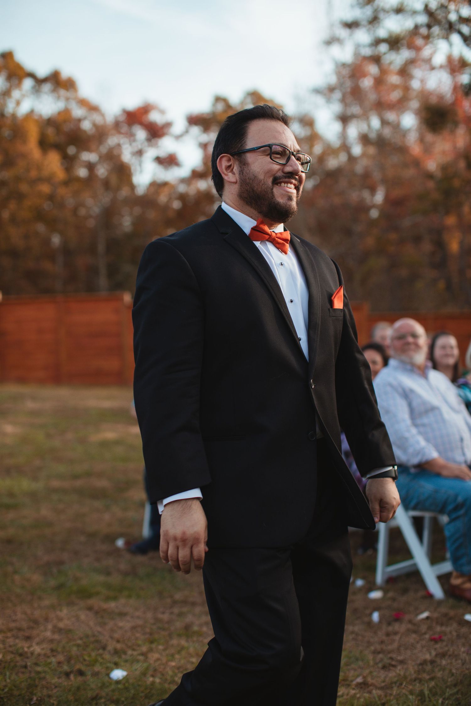 Groomsman in a black suit walking down the aisle at an outdoor ceremony