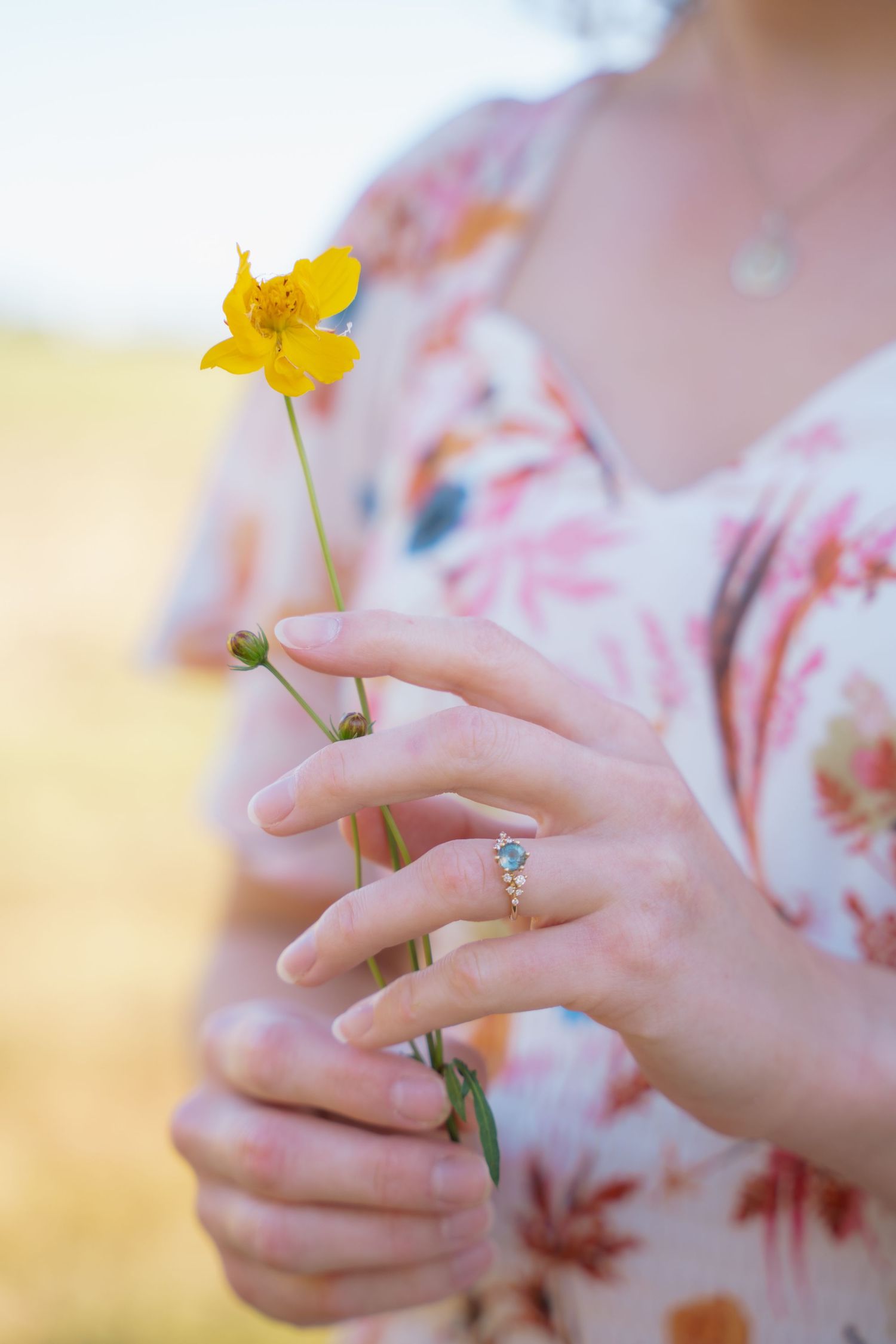 Close-up of a woman's hand with an engagement ring holding a small yellow flower