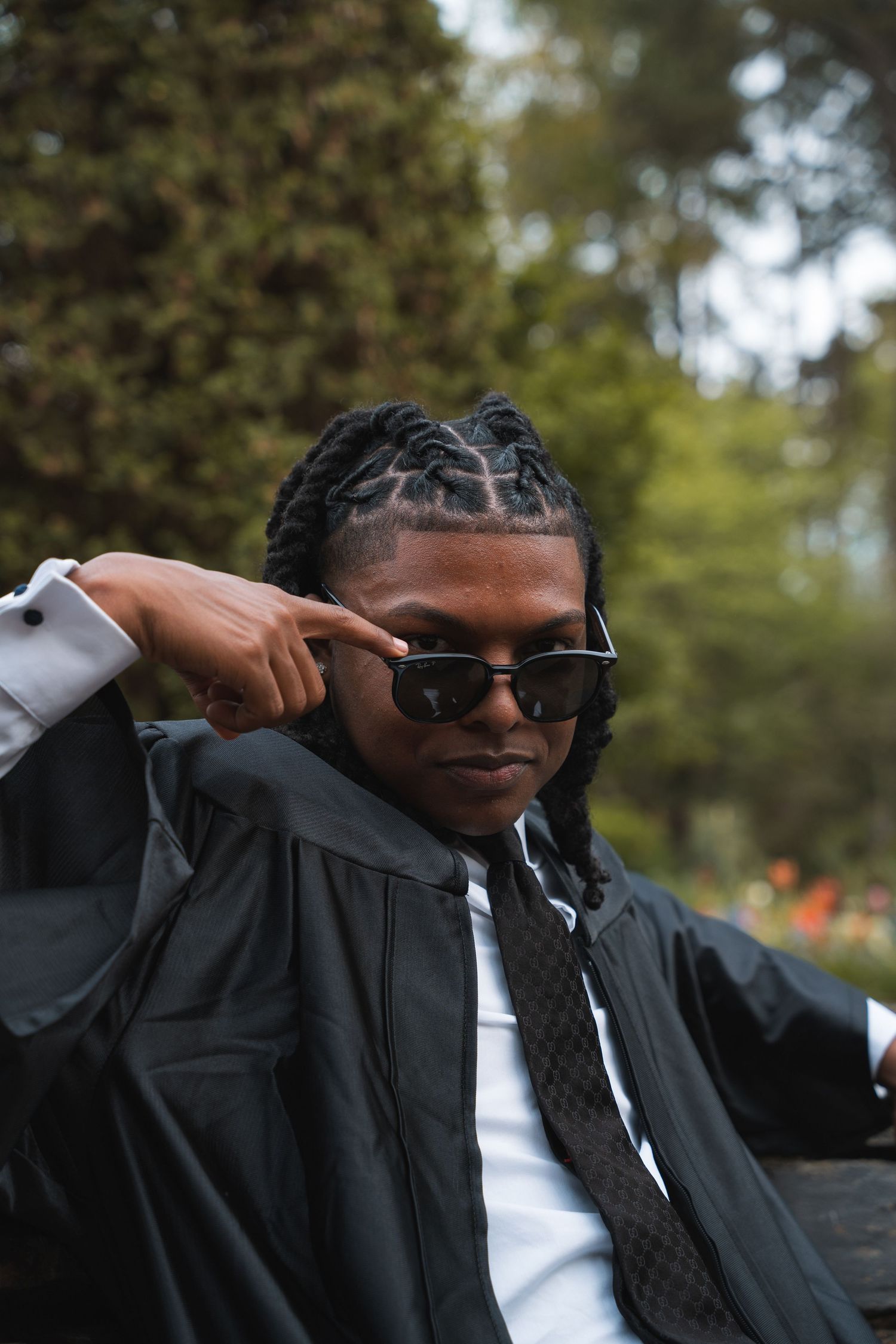 Graduate adjusting his sunglasses in his gown and tie in a lush garden