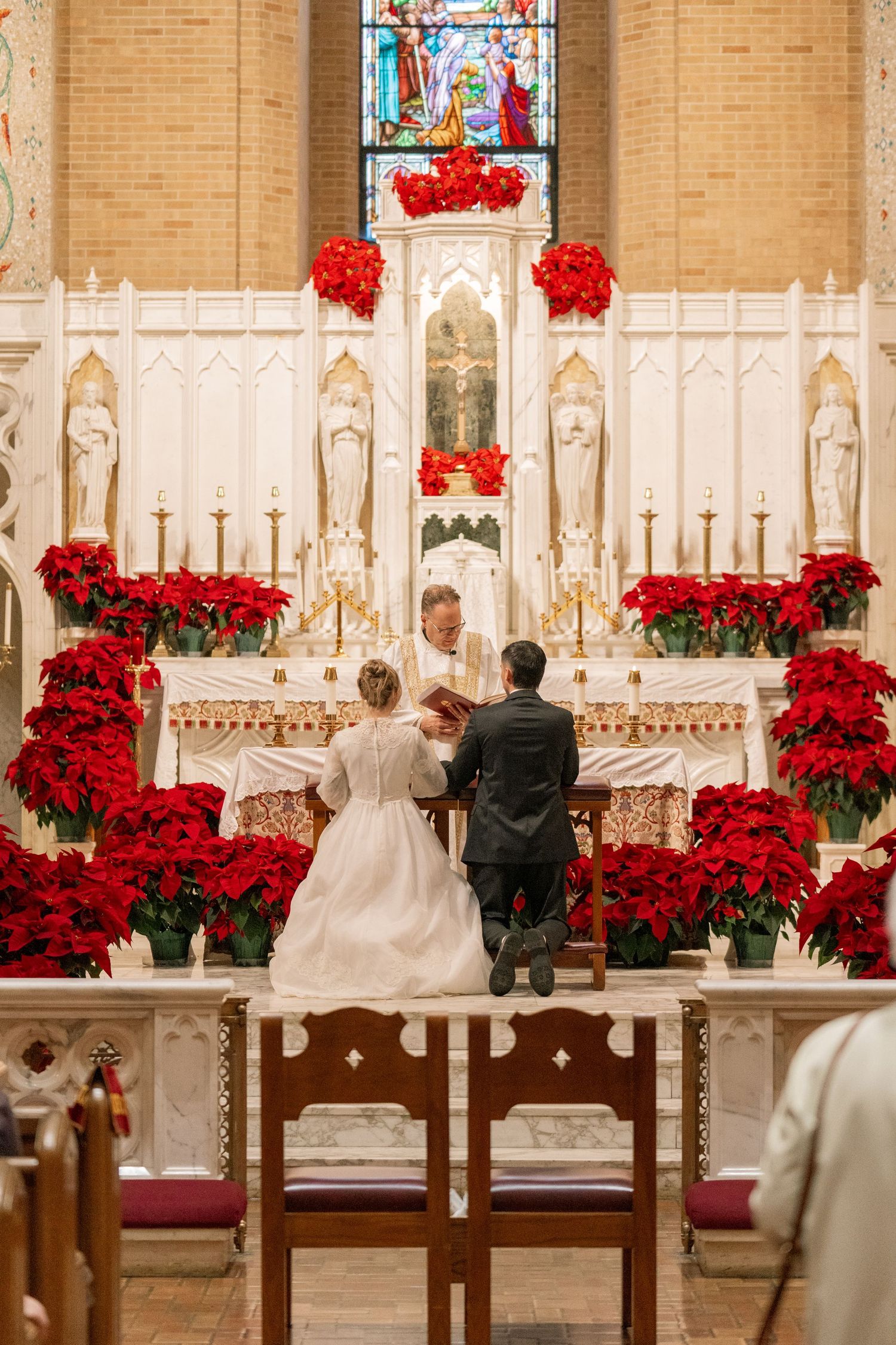 Couple kneeling at the altar framed by red poinsettias during a Nuptial Mass