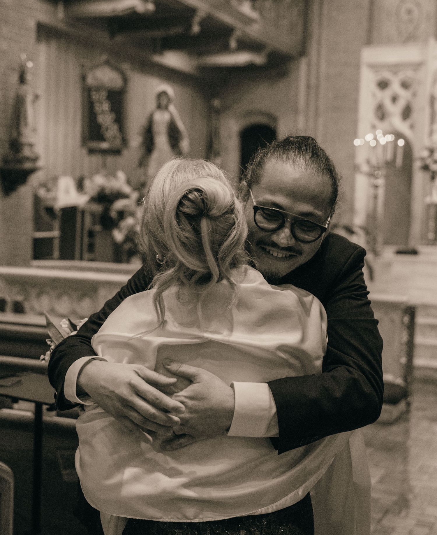 Black and white photo of a joyful hug between the bride and a loved one in church