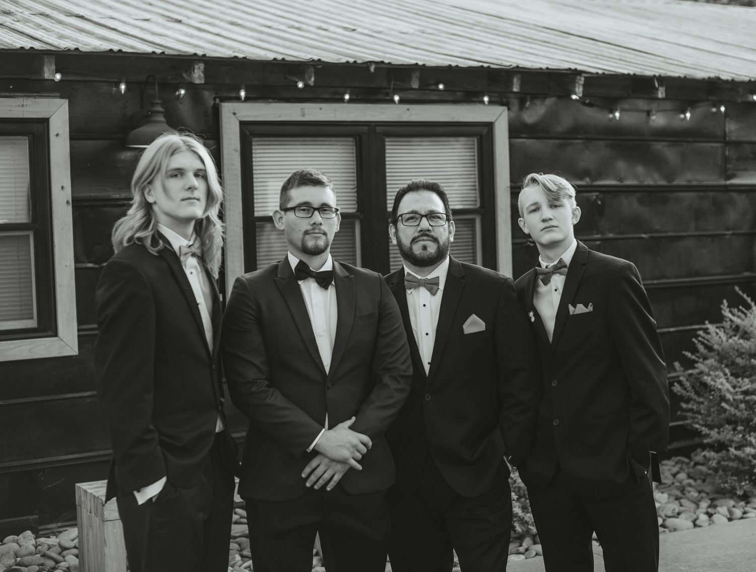 Black and white portrait of the groom and groomsmen in suits outside a barn