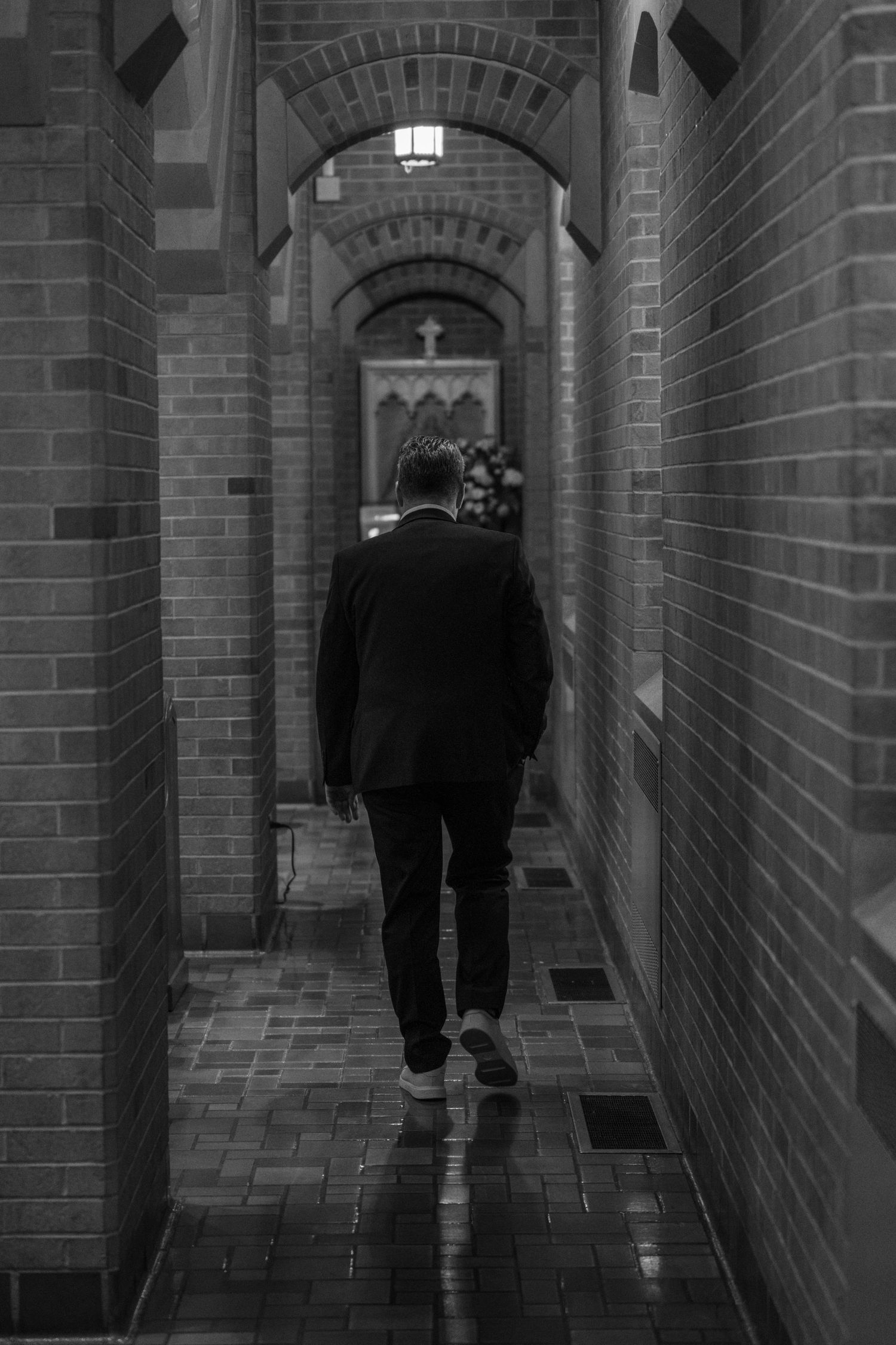 Black and white photo of the groom walking down a narrow church corridor