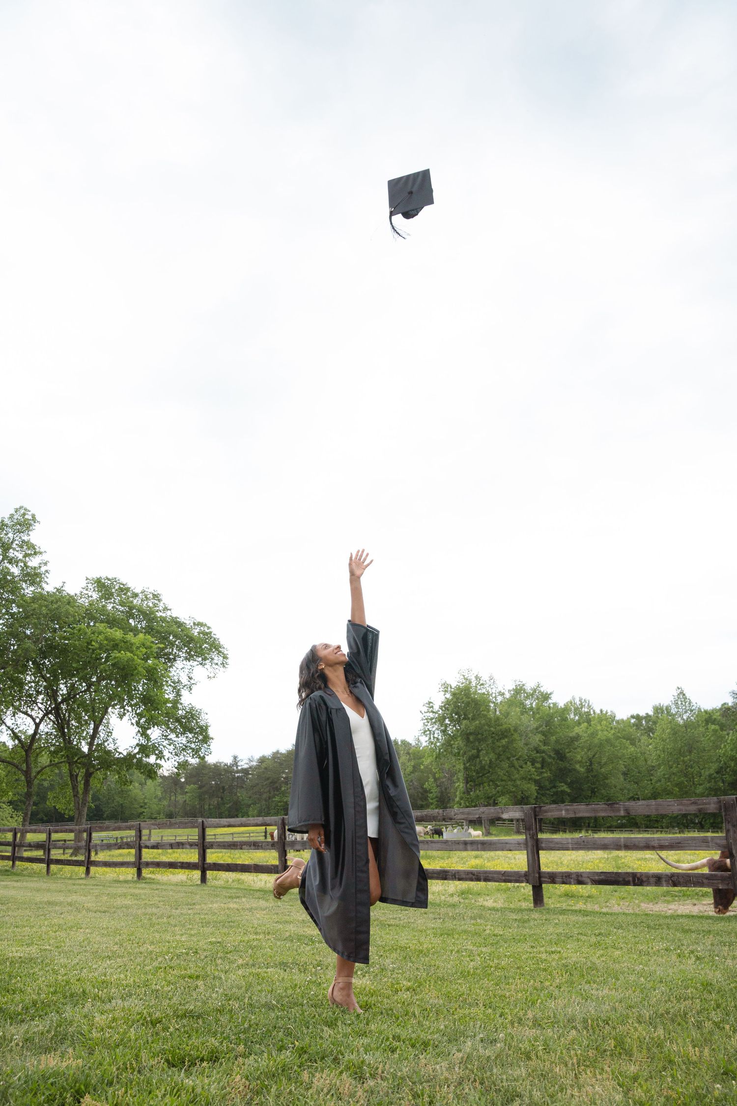 Graduate tossing her cap into the air in a wide open field