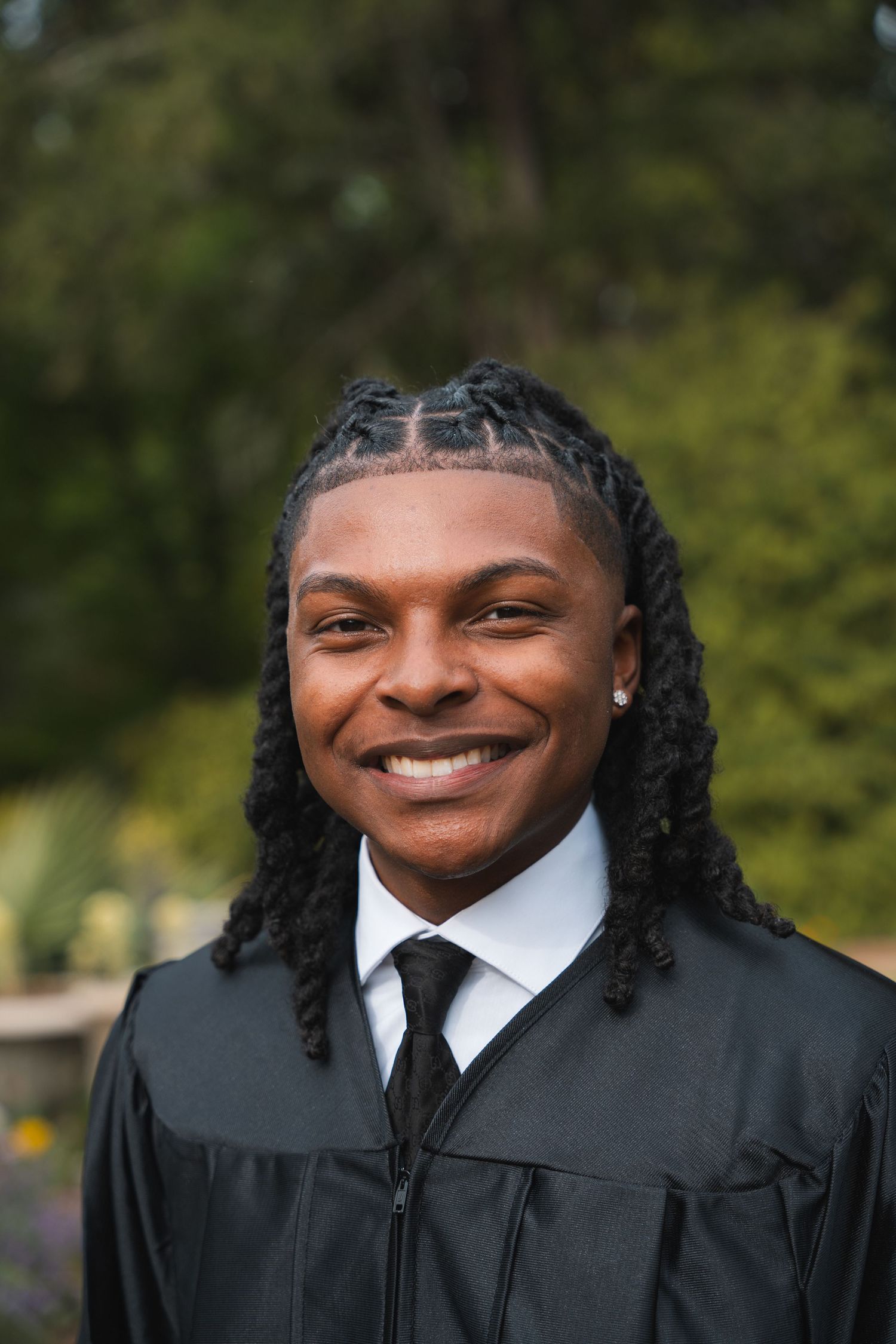 Close-up graduation portrait of a smiling young man in a black gown and tie