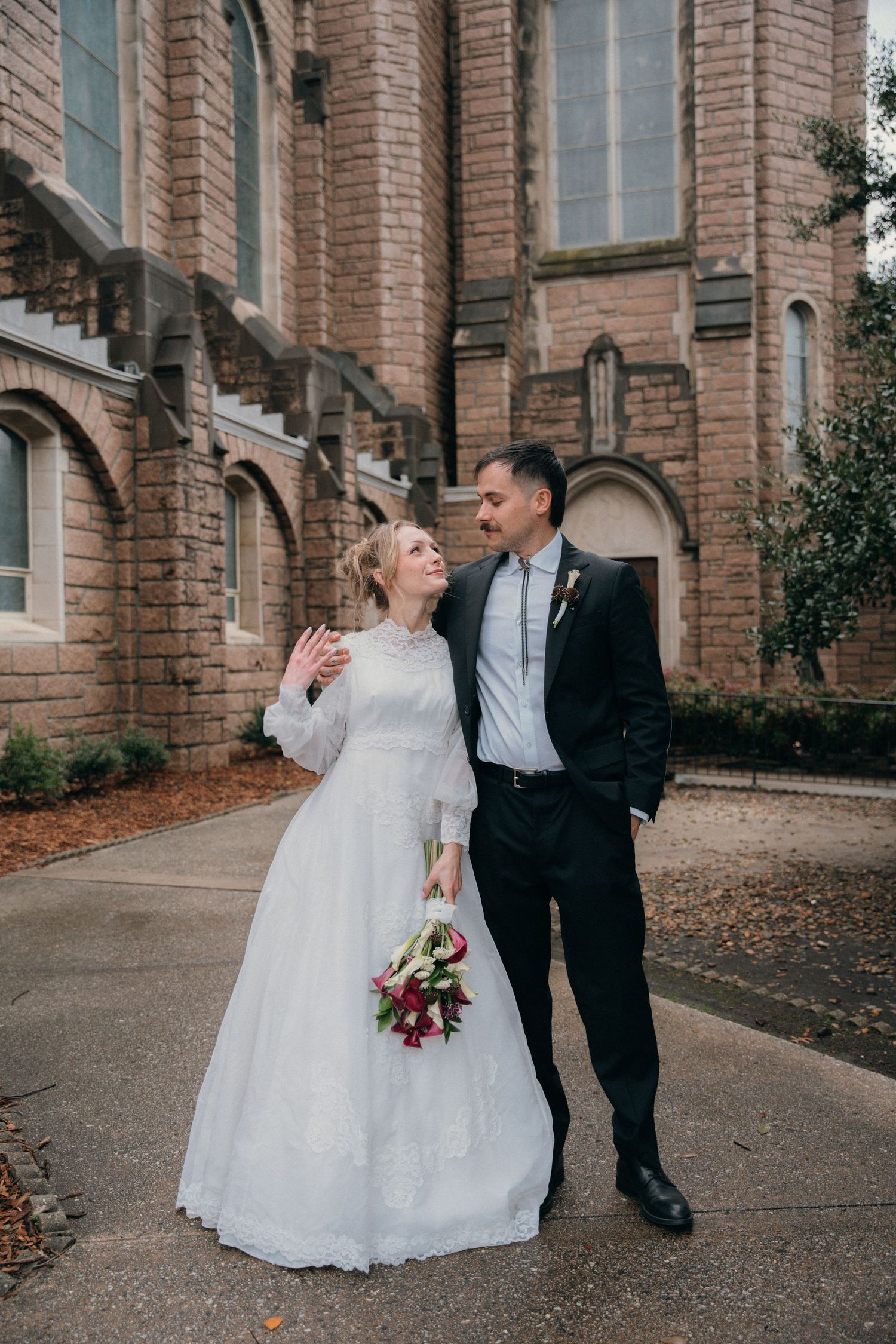Bride with a red rose bouquet and groom outside a historic church in winter