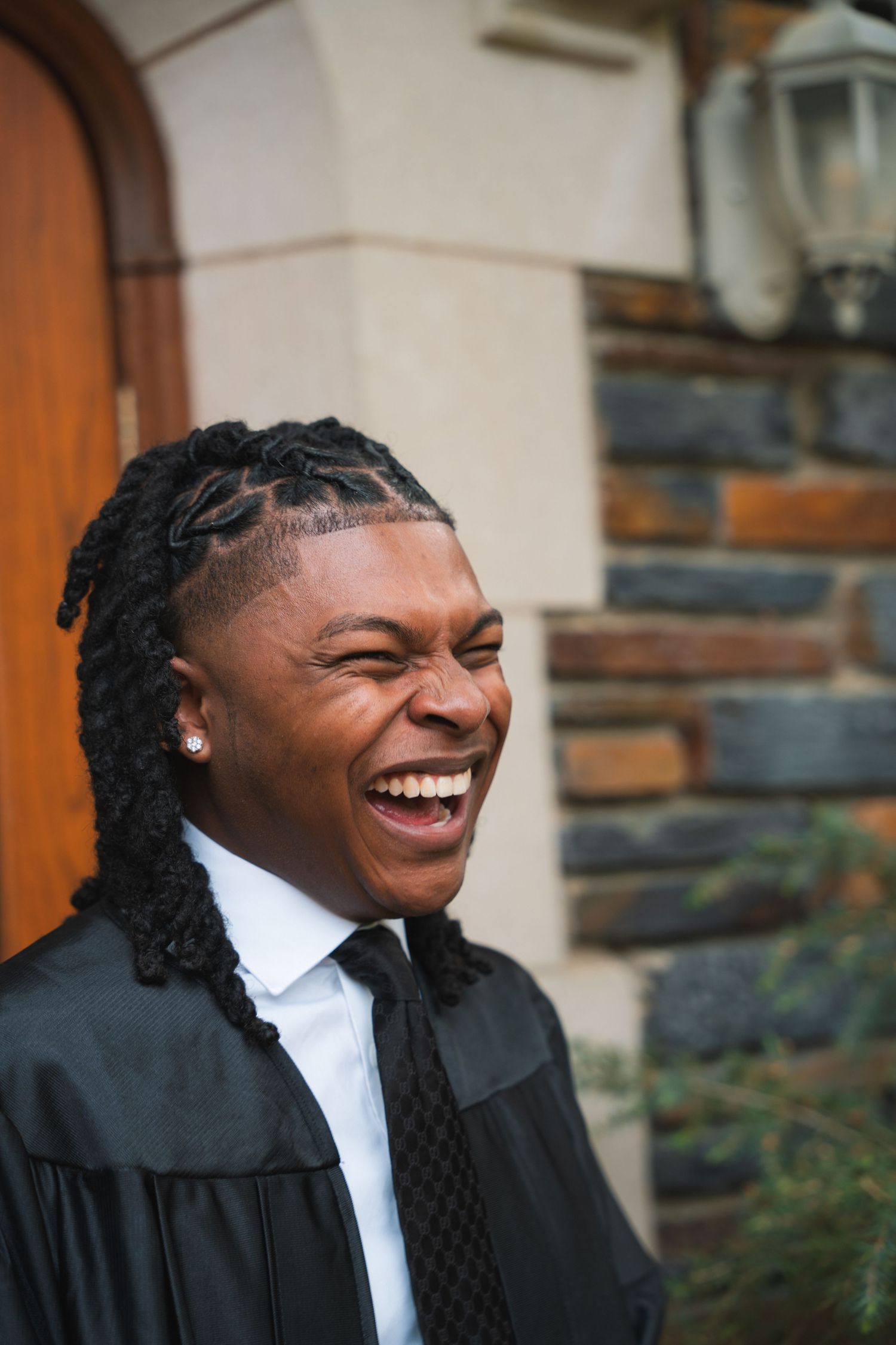 Graduate laughing in his black gown beside a stone building doorway