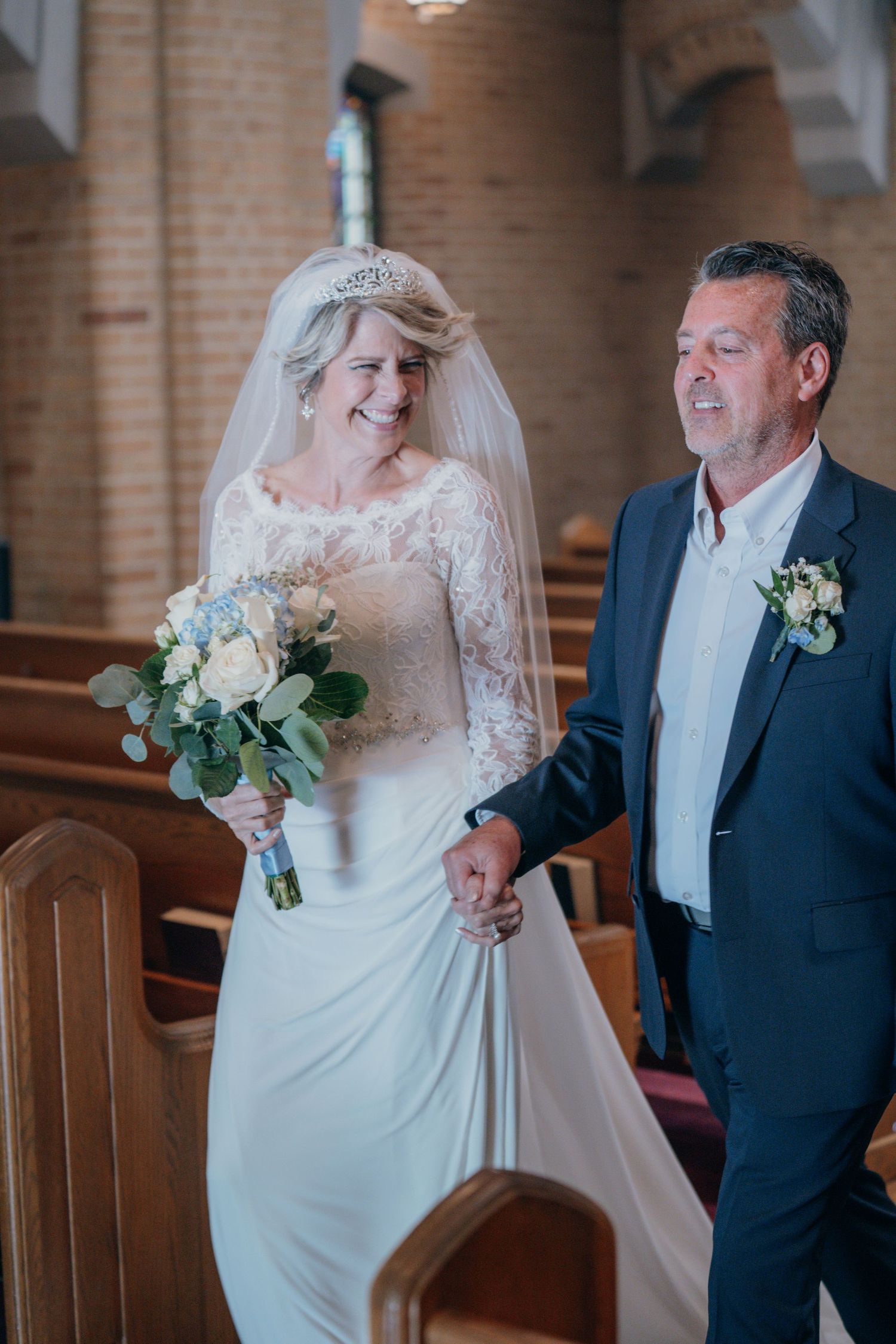 Bride in a long cathedral veil walking down the aisle with her father