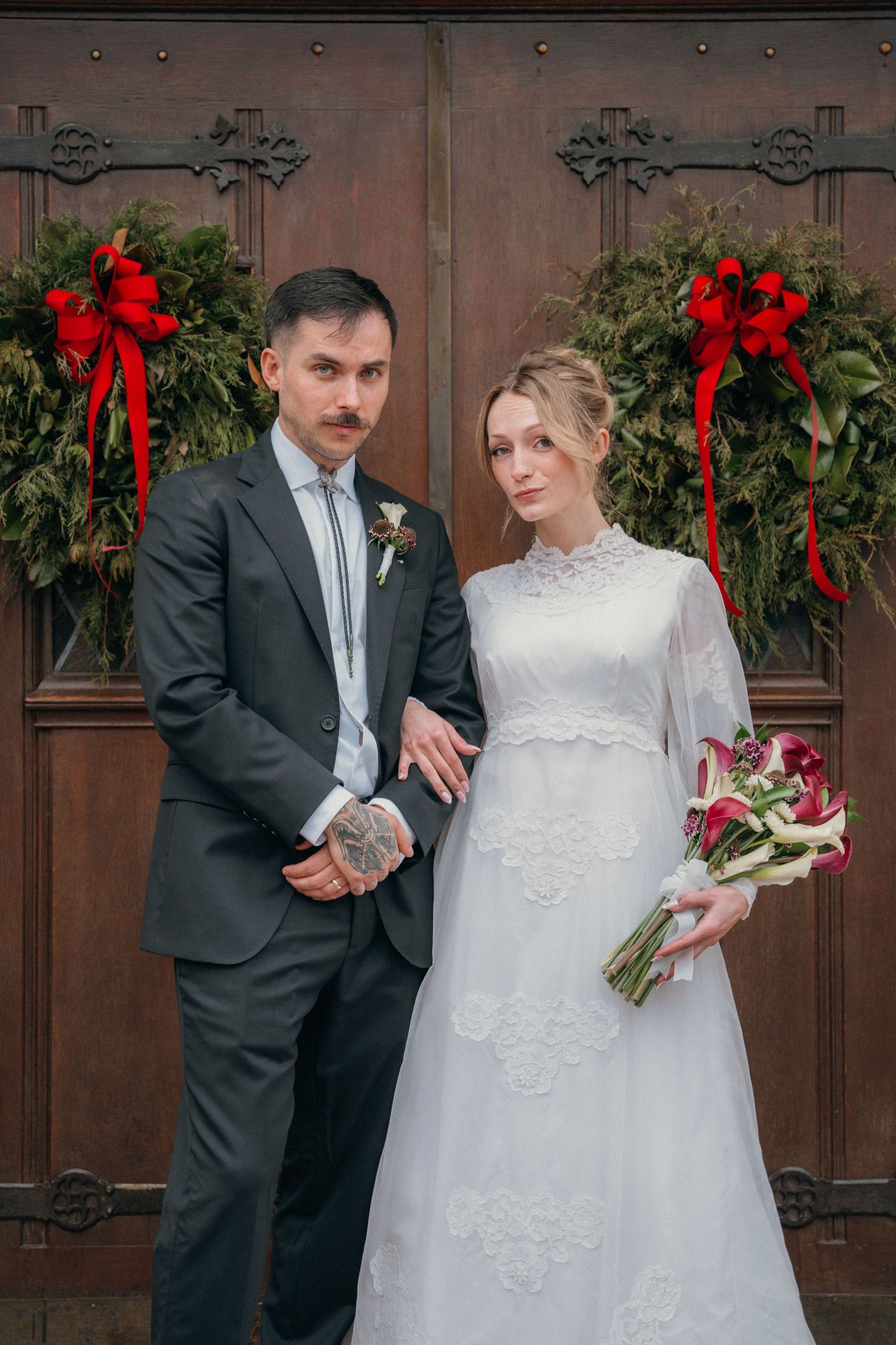 Bride and groom standing at wreath-covered church doors after their Christmas wedding
