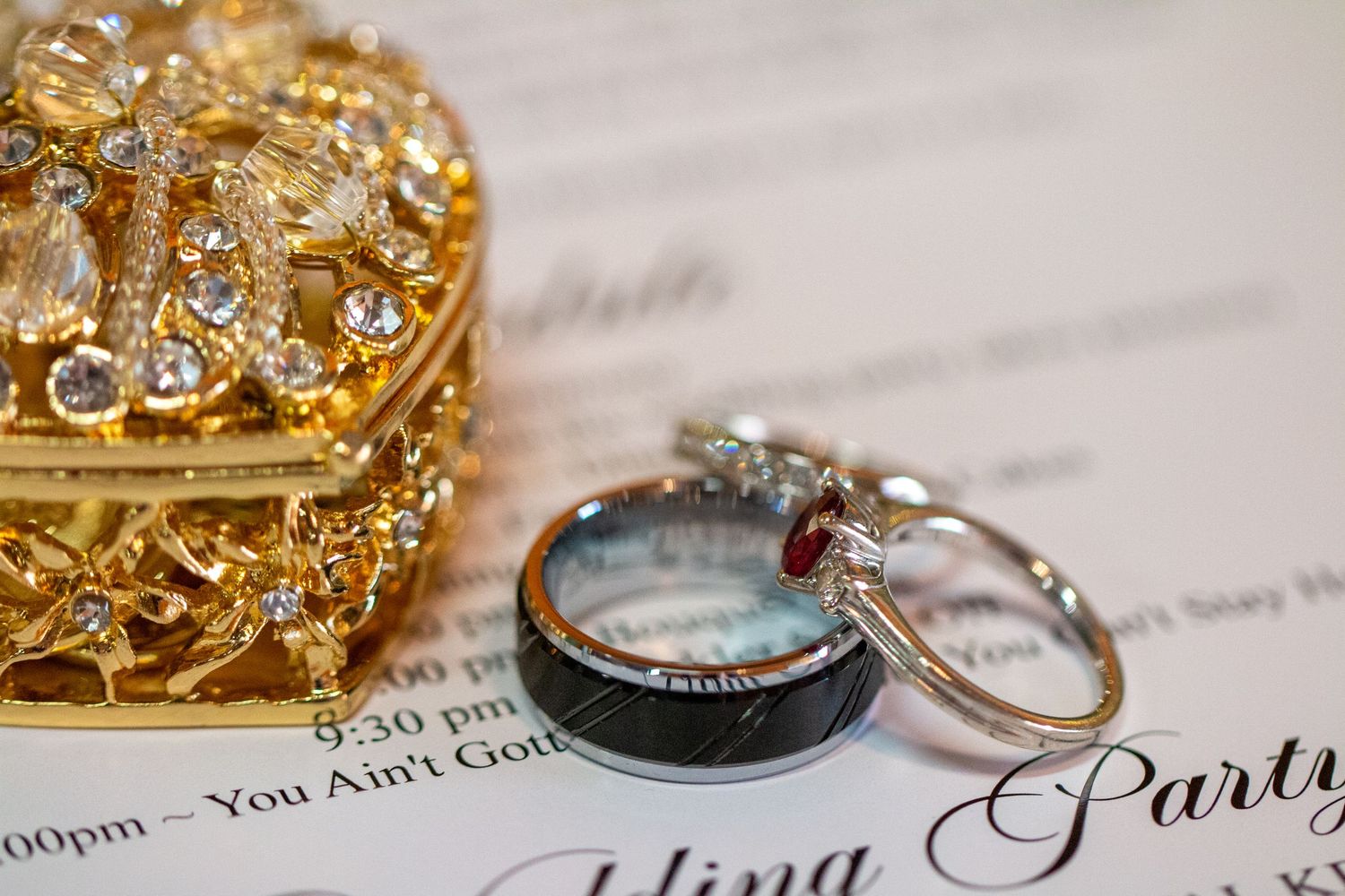 Wedding rings resting on the invitation beside an ornate gold ring box