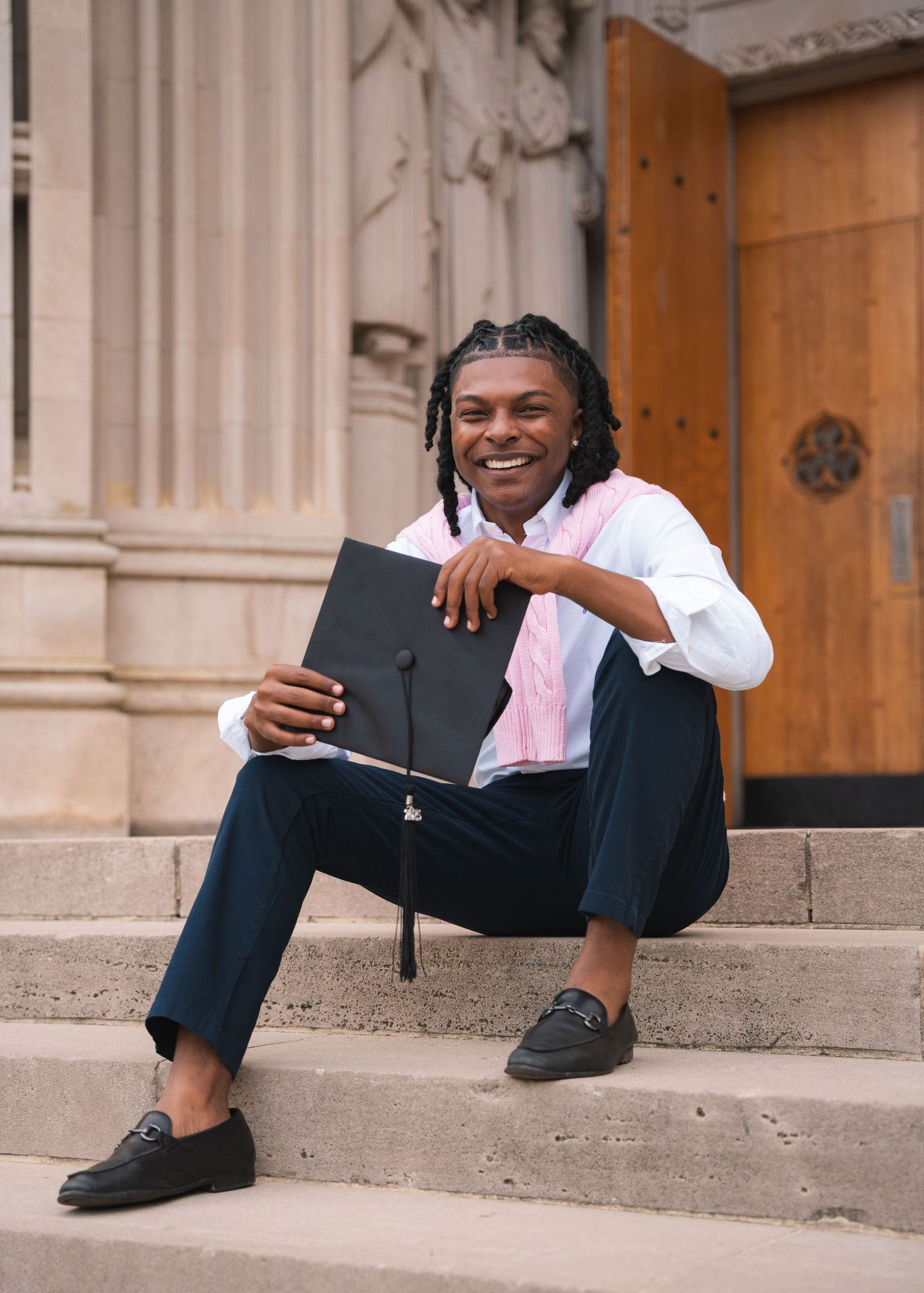 Graduate sitting on the stone steps of a Gothic chapel holding a Bible