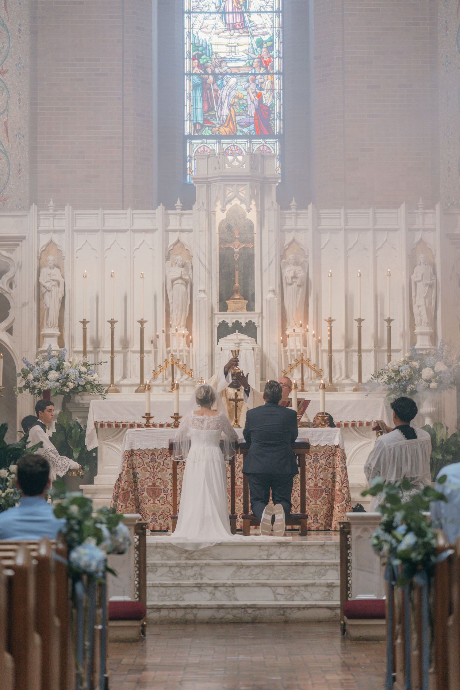 Wide view down the aisle of a Catholic wedding Mass beneath stained glass