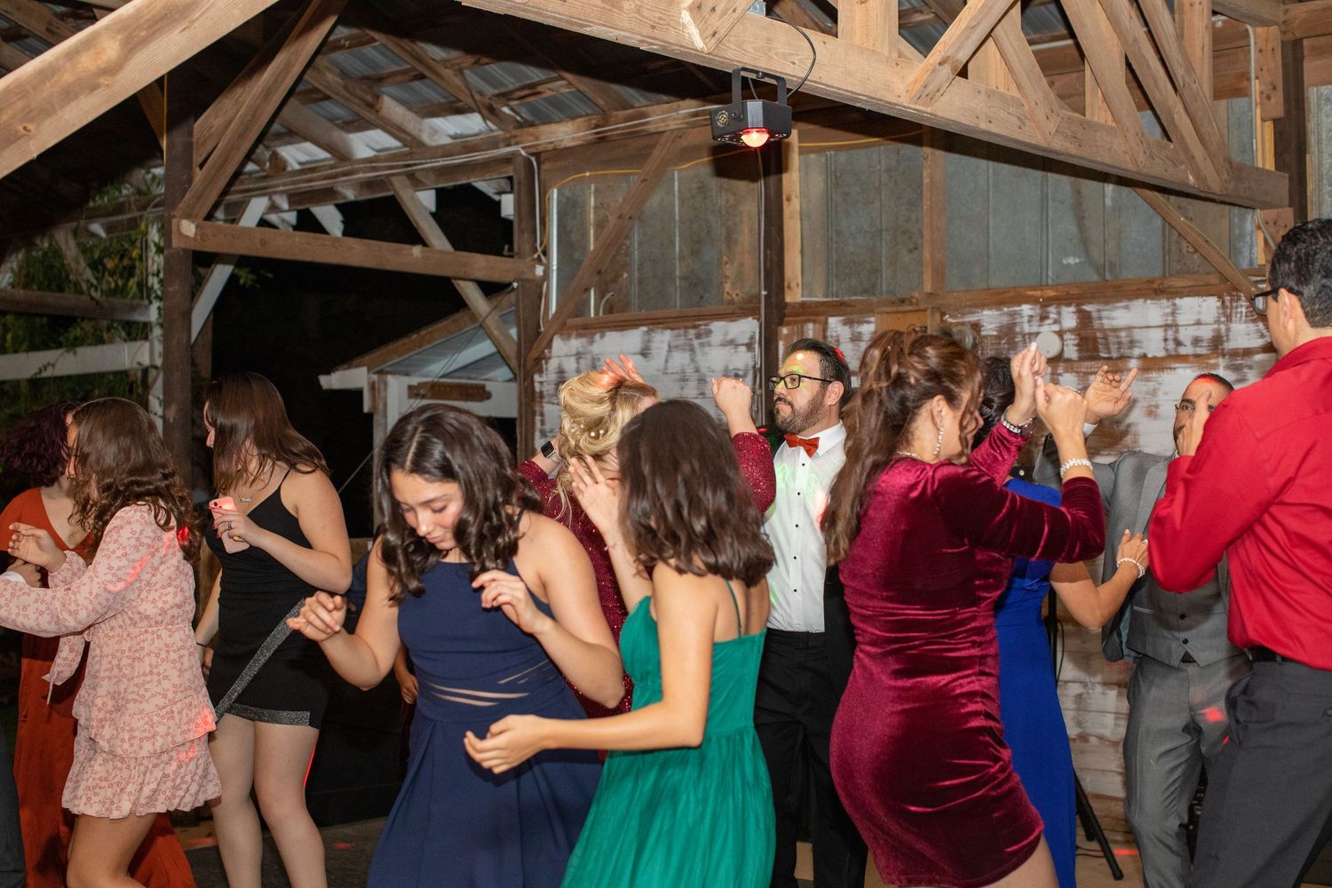 Packed dance floor of wedding guests inside a wooden barn