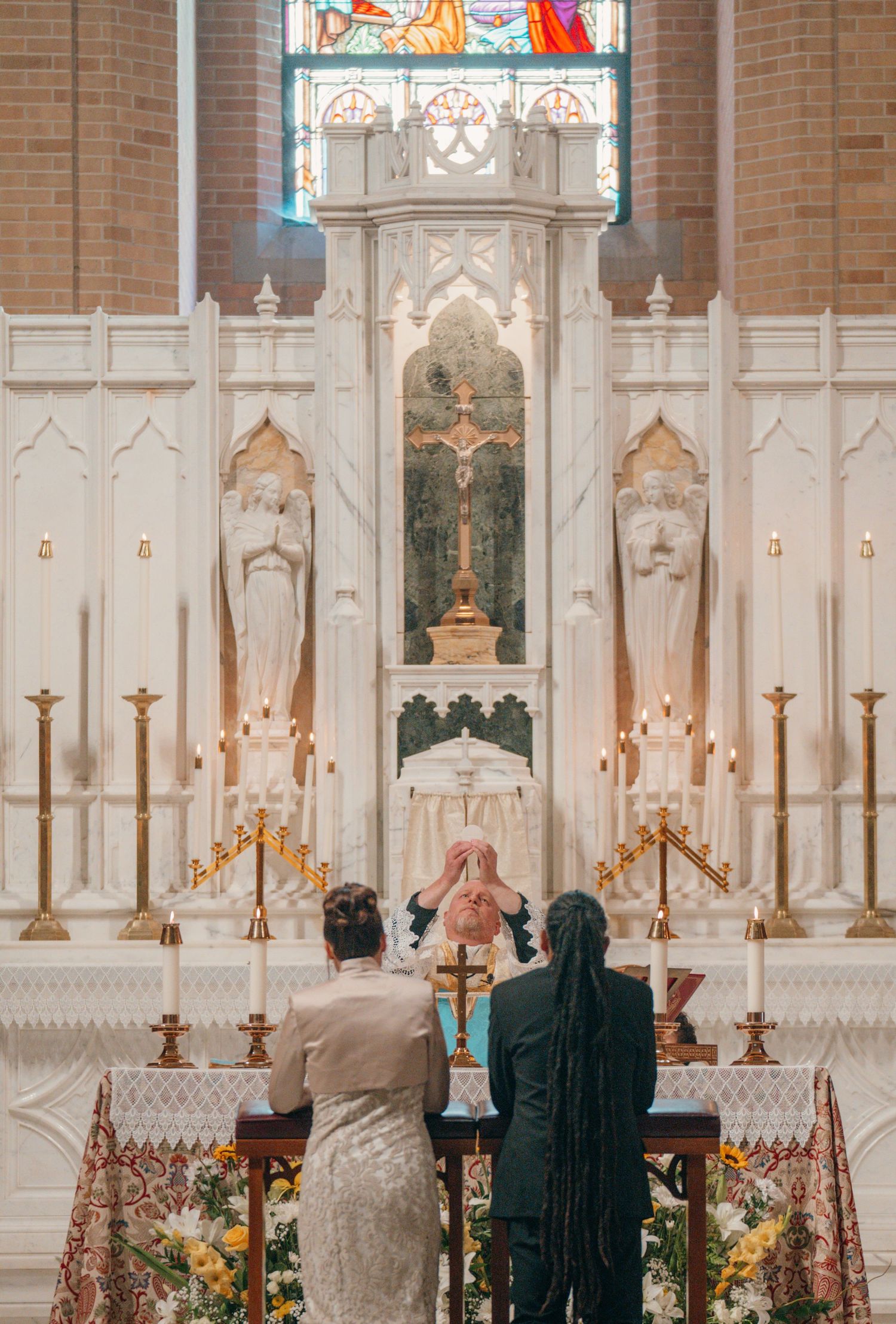 Bride and groom kneeling at the altar rail beneath a Gothic high altar