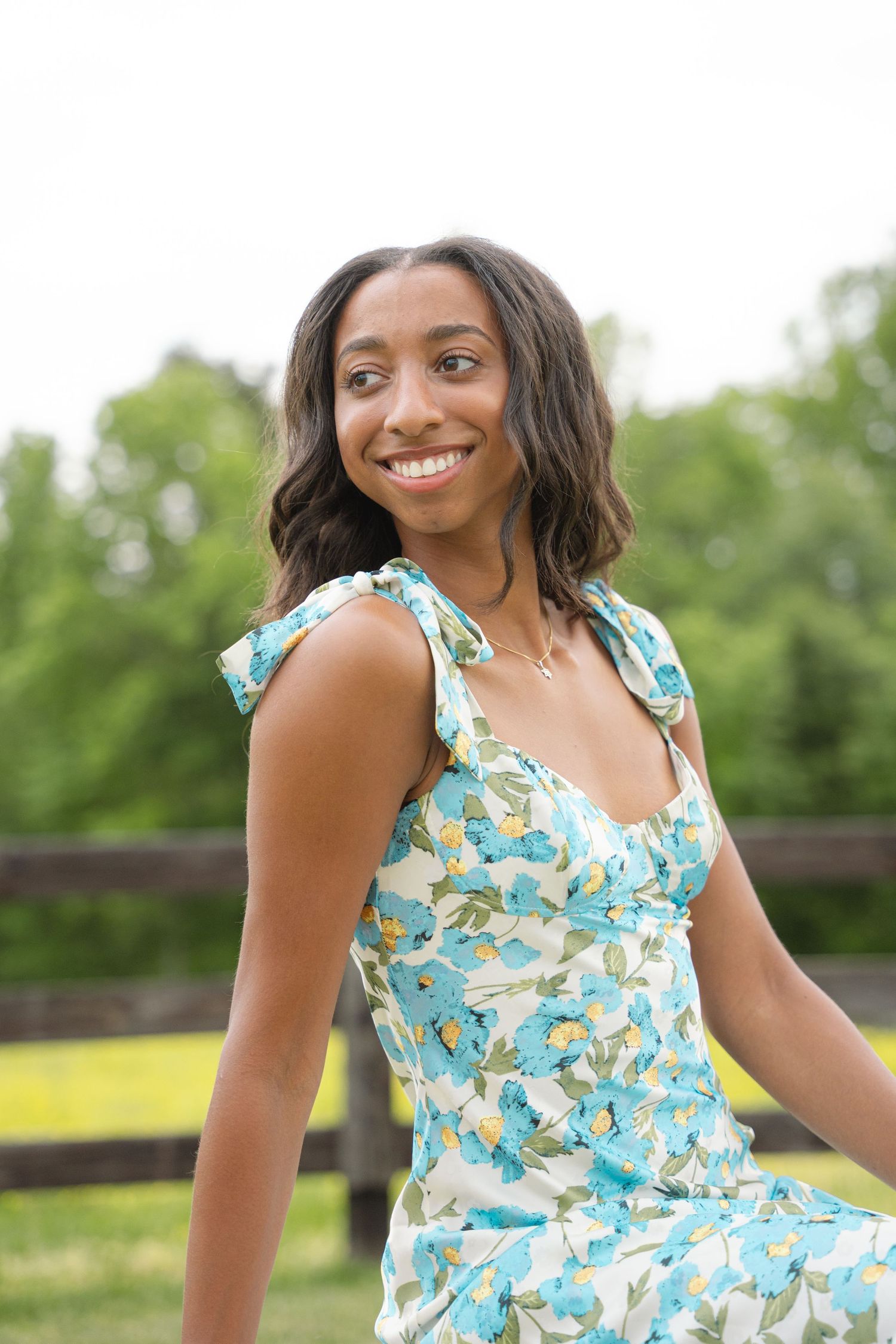 Smiling graduate in a floral sundress looking over her shoulder in a summer field