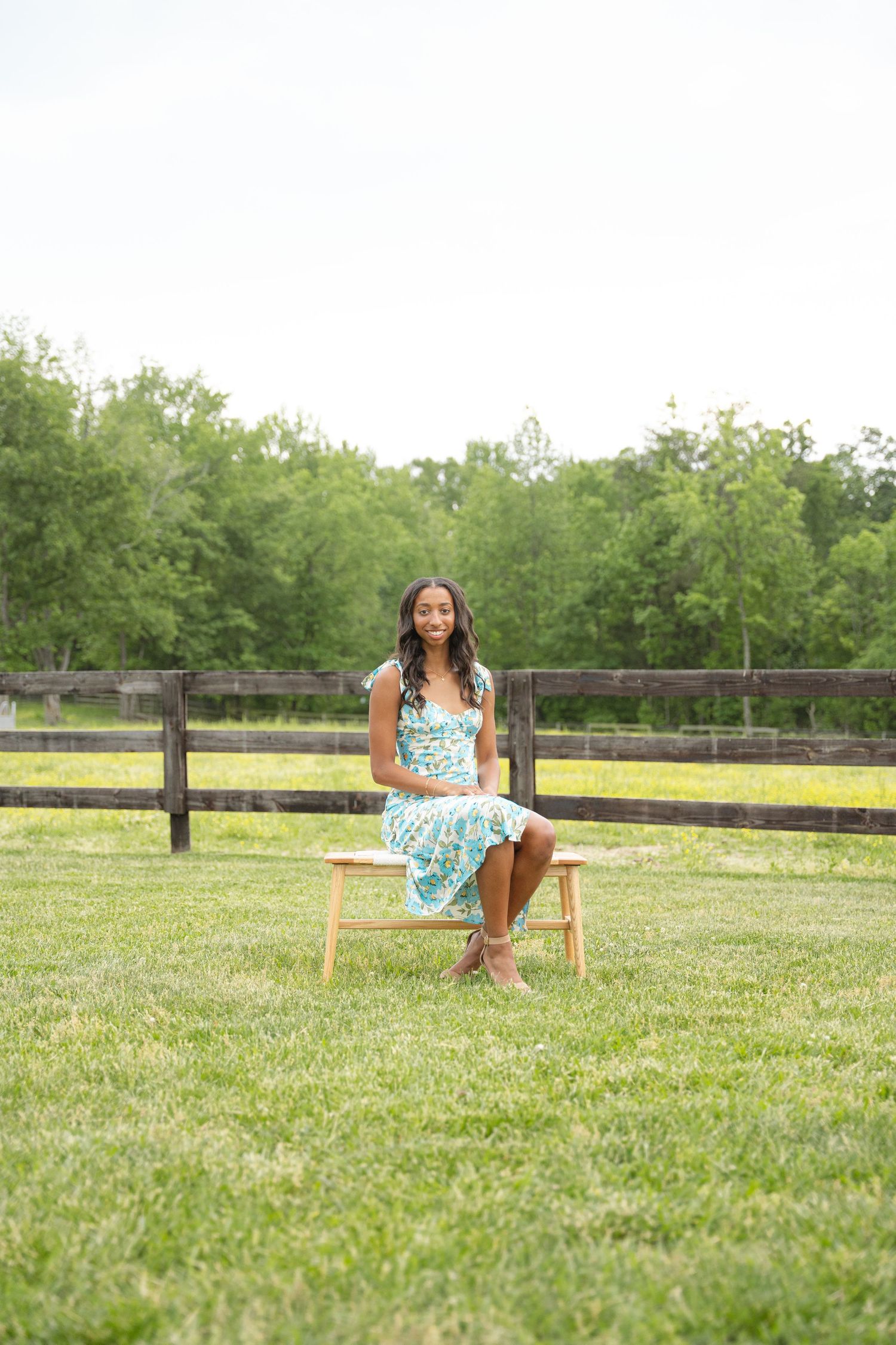 Senior portrait of a graduate sitting on a wooden stool in an open green field