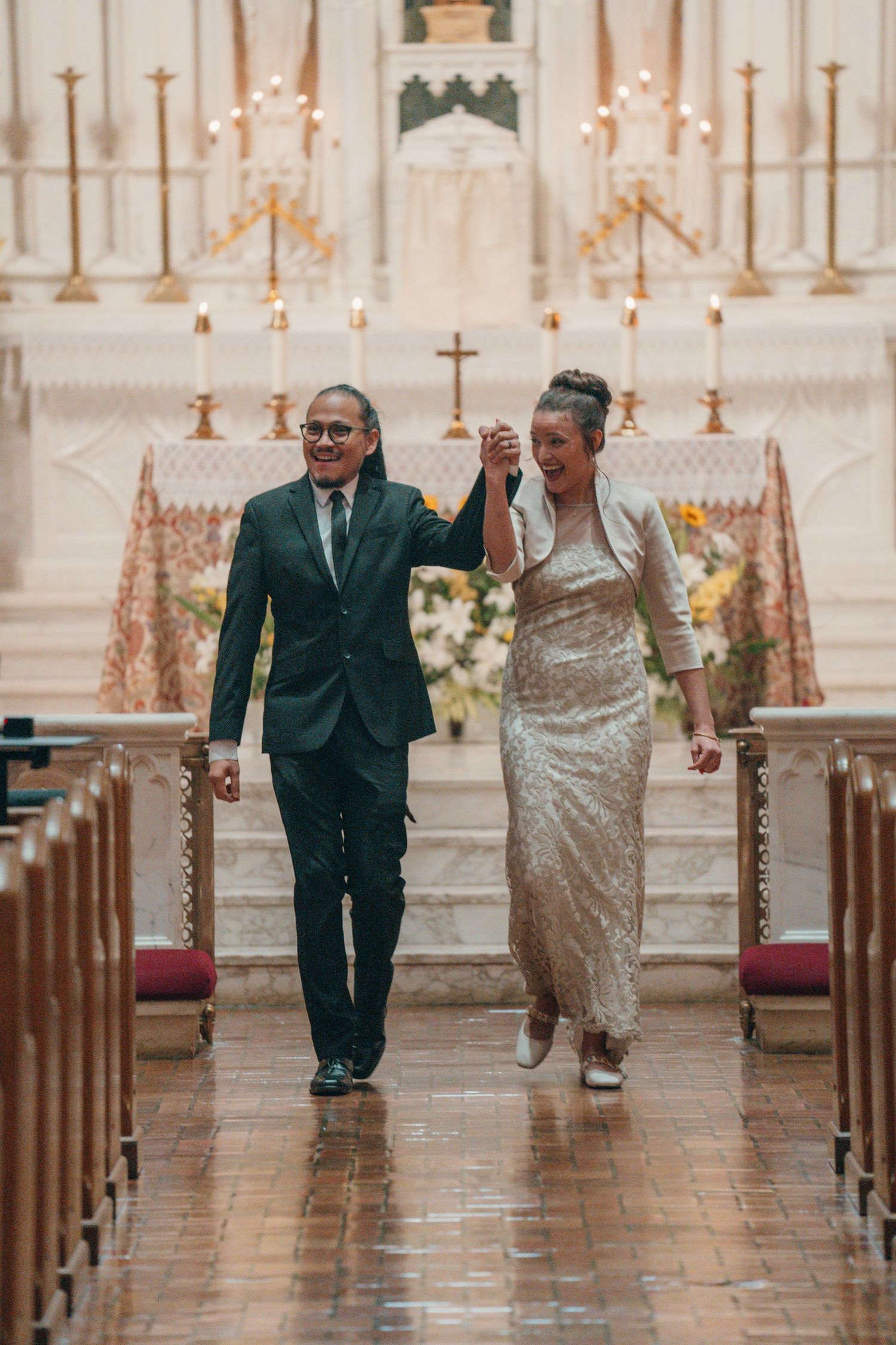 Newlyweds recessing down the aisle of a Catholic church with a white marble altar