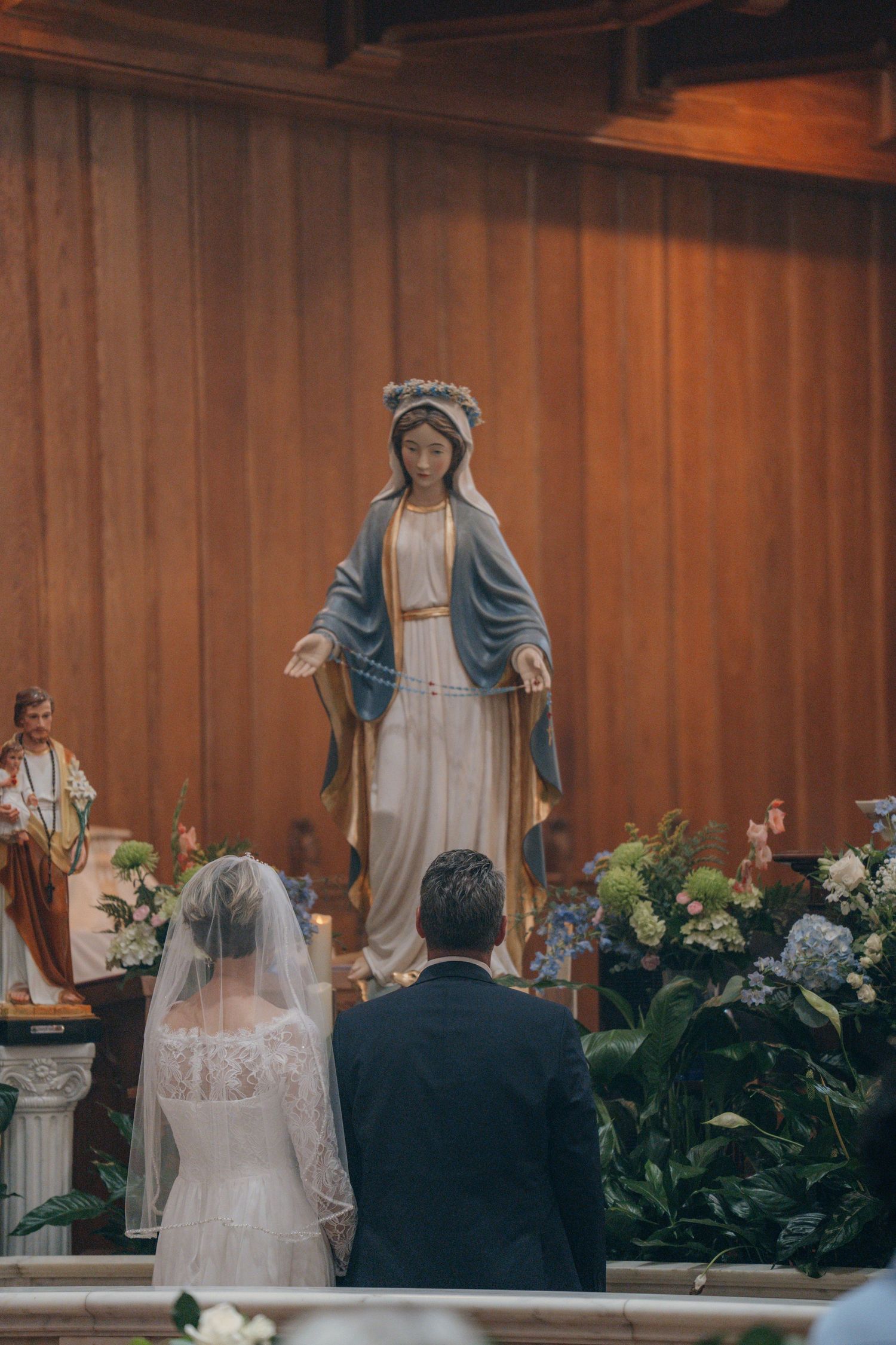 Couple kneeling before a statue of the Blessed Virgin Mary after their vows